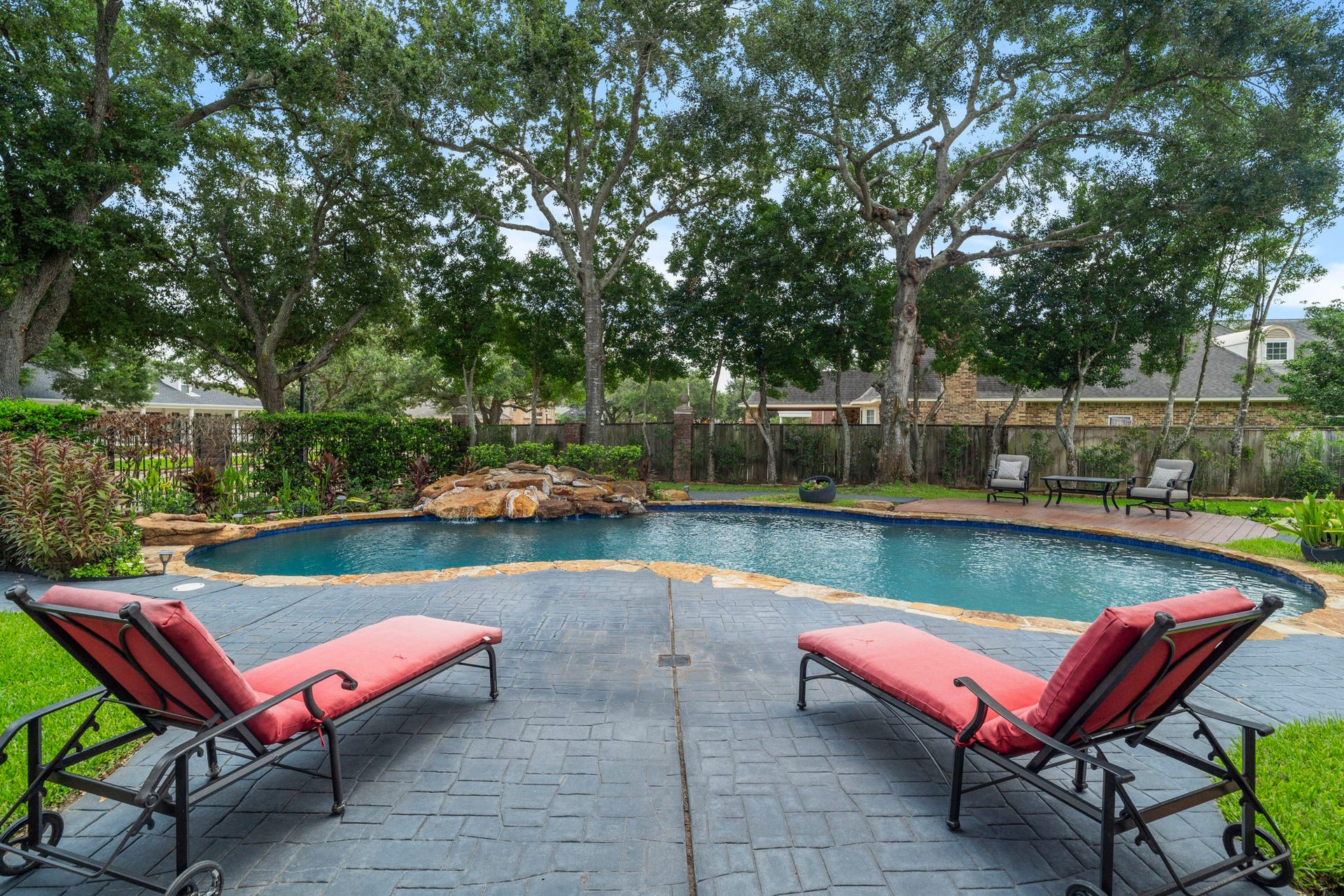 The pool is framed by mature shade trees and beautifully maintained landscaping, offering a tranquil retreat with a sense of privacy.