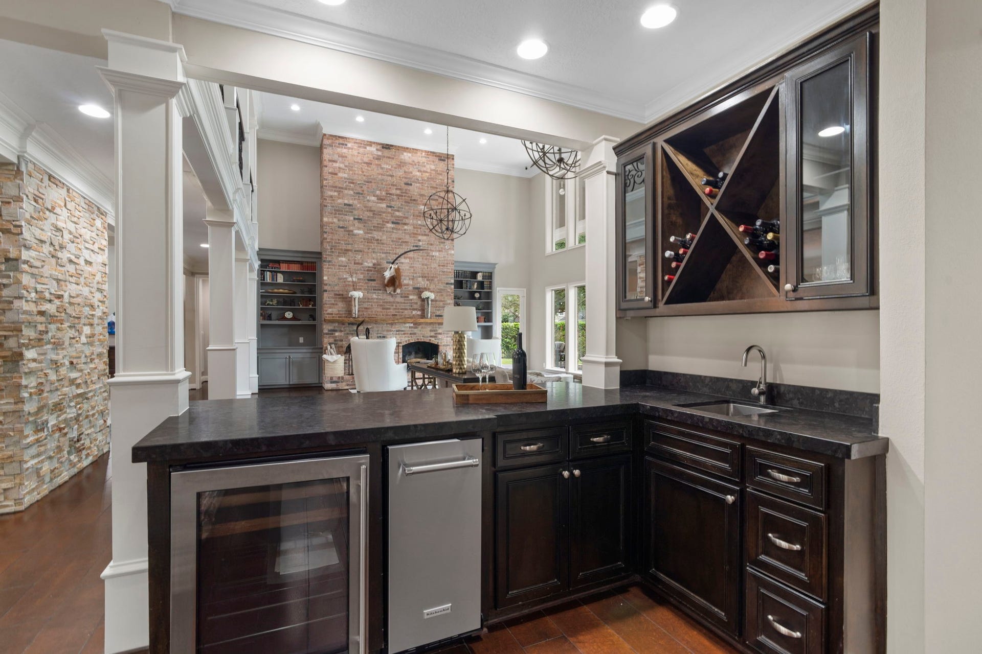 The fully equipped bar features a sink, new ice maker, U-Line beverage cooler, wine rack, glass-front display cabinetry, and generous counter space. An impressive 14 sinks are thoughtfully incorporated throughout the home!