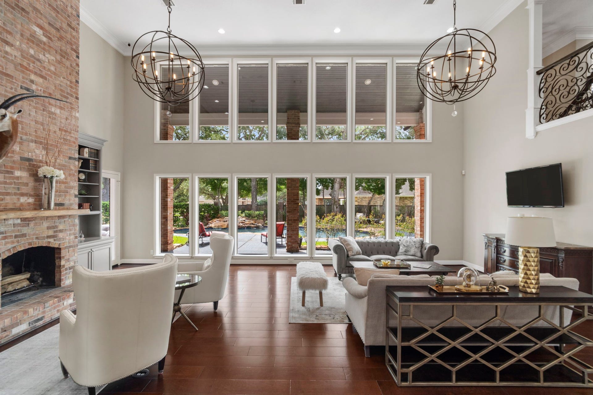 Architectural character defines the living room with a two-story exposed brick fireplace, custom built-in cabinetry, while statement globe chandeliers add a touch of modern elegance.