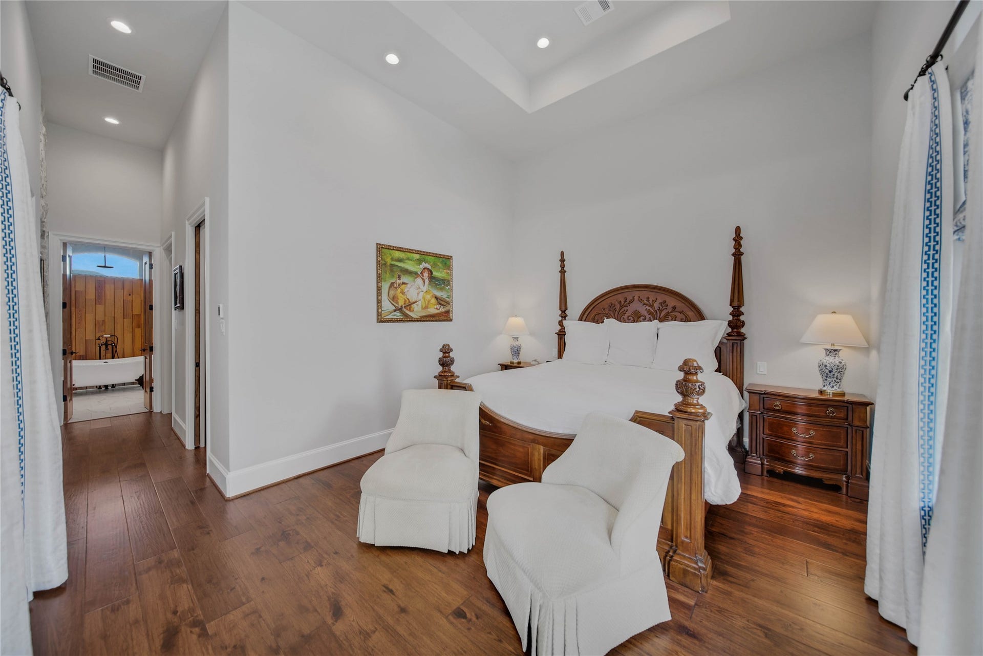 24718 Shadow Pond Drive, Spring, TX 77389 Spacious bedroom with elegant wood flooring, a luxurious four-poster bed, and cozy seating, leading to a charming ensuite bathroom with a classic freestanding tub.