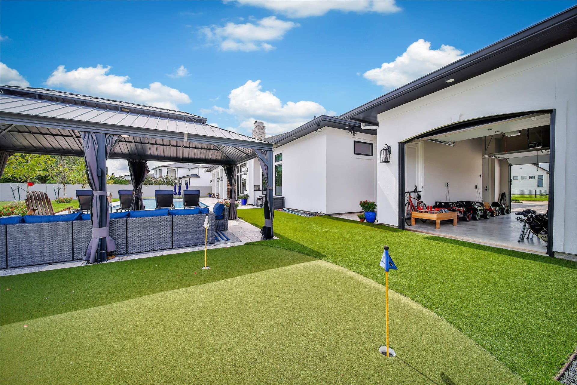 24718 Shadow Pond Drive, Spring, TX 77389 Experience luxury outdoor living with a covered patio featuring a stylish seating area, a pristine putting green, and an open garage offering ample space for recreational activities.