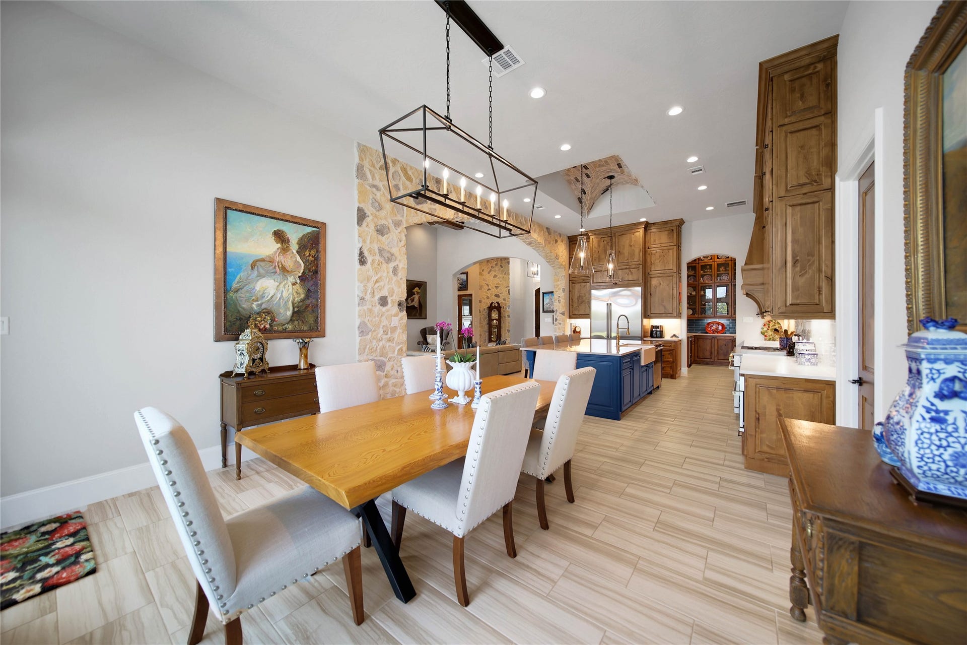 24718 Shadow Pond Drive, Spring, TX 77389 Elegant open-concept dining and kitchen area featuring a spacious wooden dining table, modern lighting, and a stylish kitchen with a stone accent wall, blue island, and rich wooden cabinetry.