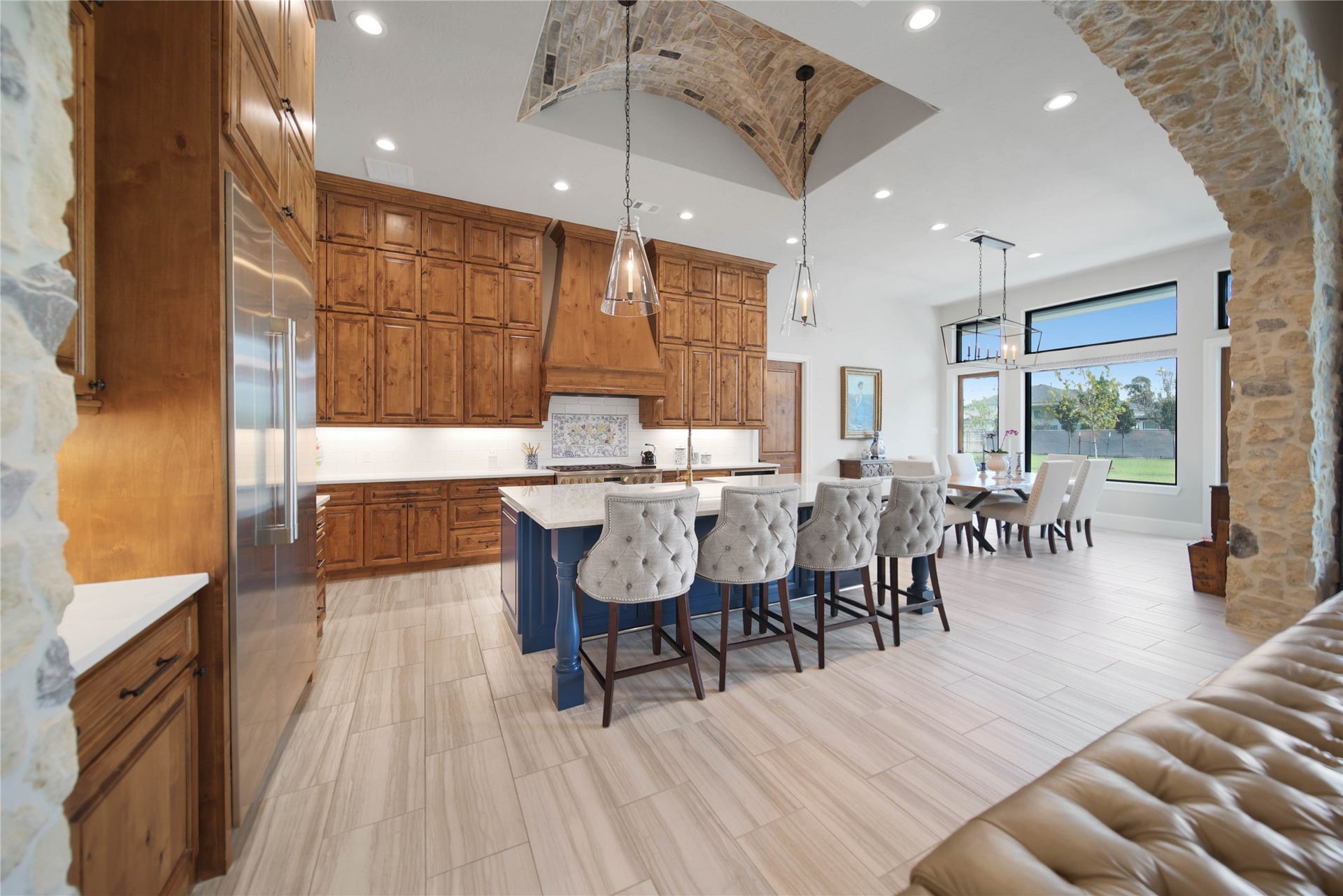 24718 Shadow Pond Drive, Spring, TX 77389 Stunning kitchen with rich wood cabinetry, a large central island with elegant seating, and a cozy dining area framed by expansive windows, perfect for enjoying natural light and serene views.