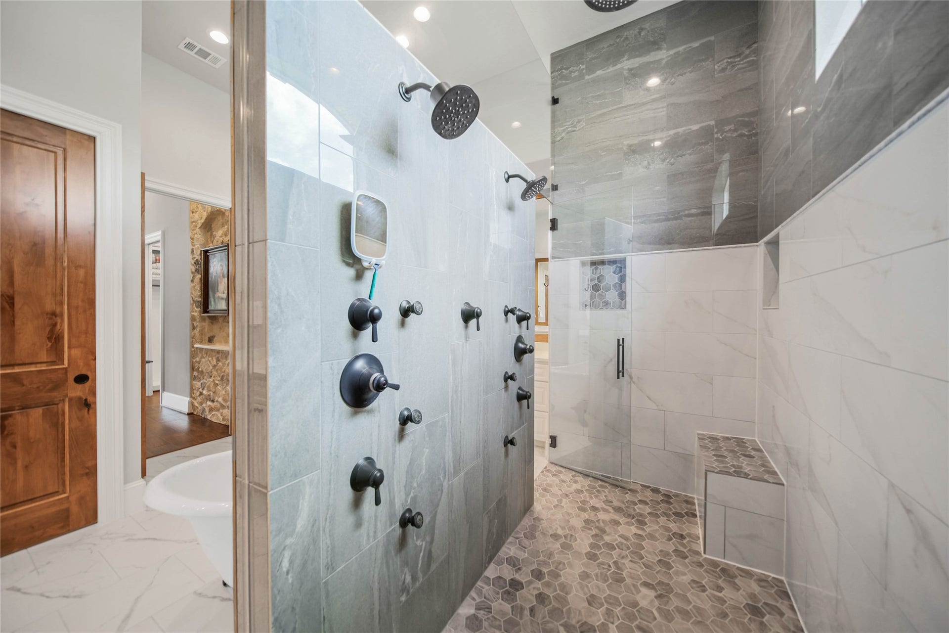 24718 Shadow Pond Drive, Spring, TX 77389 Luxurious walk-in shower featuring dual rain showerheads, elegant tile work, and a built-in bench for ultimate relaxation.