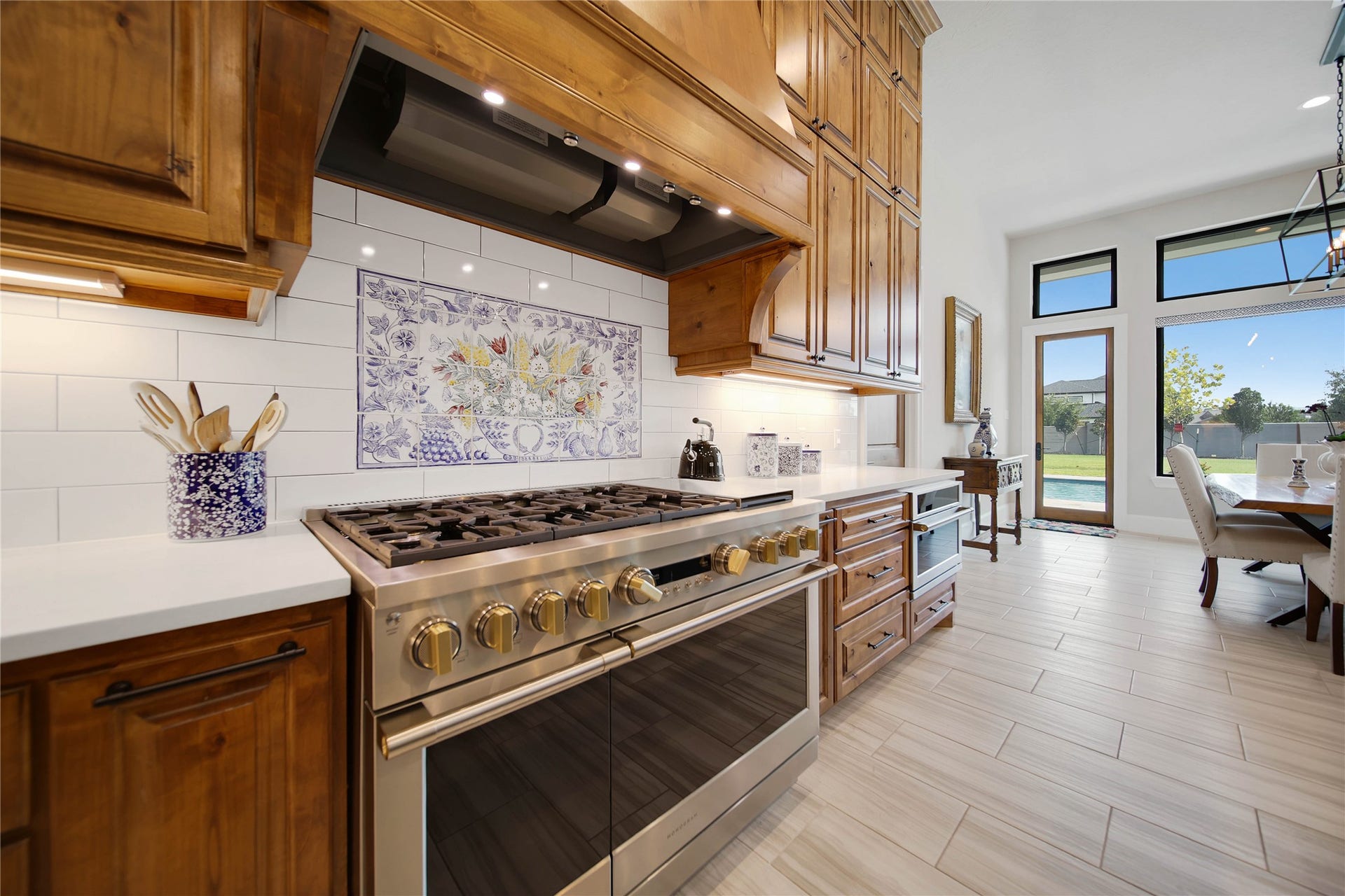 24718 Shadow Pond Drive, Spring, TX 77389 Elegant kitchen featuring a high-end stainless steel gas range, beautiful wood cabinetry, and a charming tile backsplash, opening into a bright dining area with large windows overlooking the backyard.