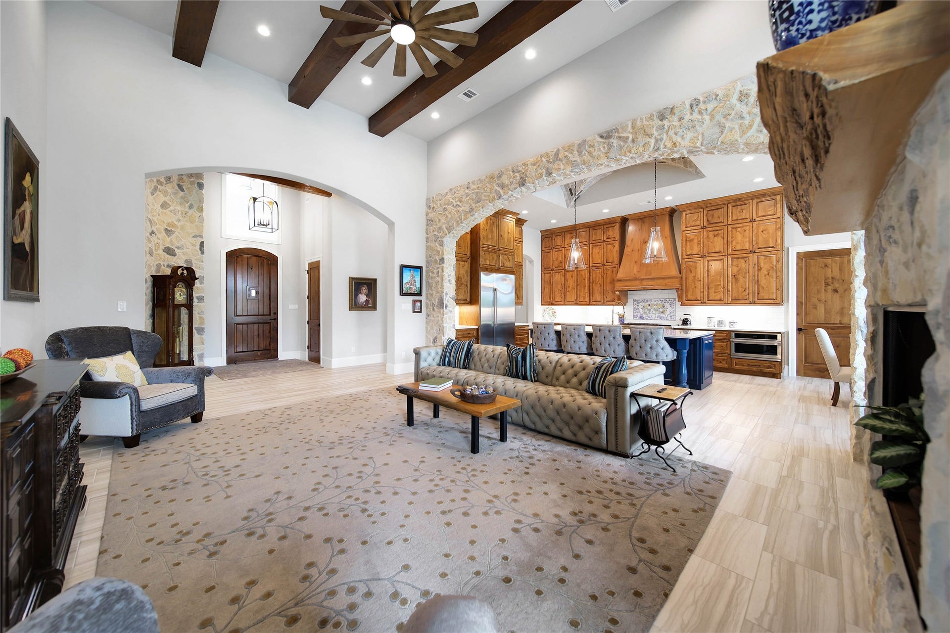24718 Shadow Pond Drive, Spring, TX 77389 Stunning open-concept living area featuring high ceilings with wooden beams, a cozy stone fireplace, and a seamless flow into the gourmet kitchen with rich wood cabinetry and a large island.