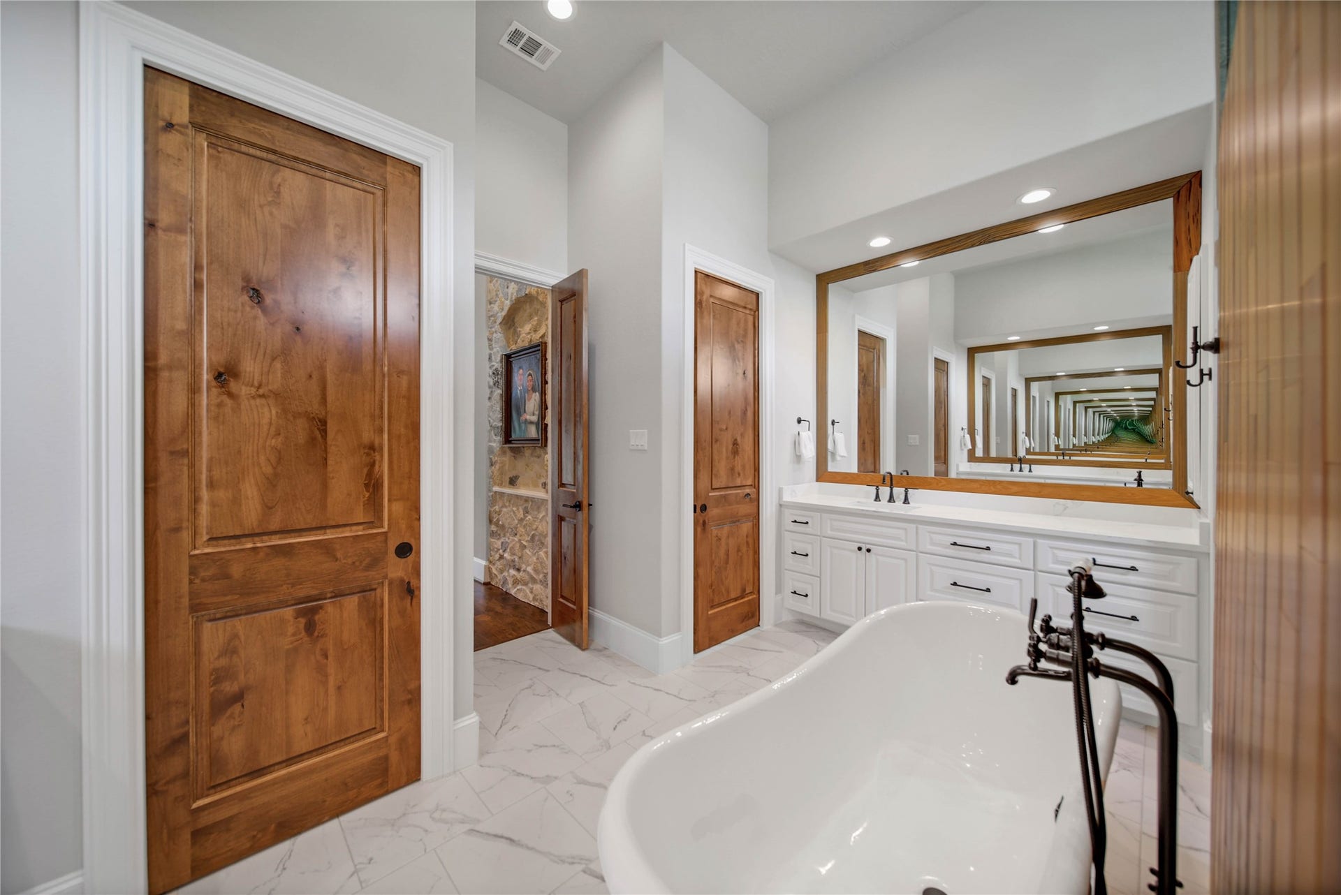 24718 Shadow Pond Drive, Spring, TX 77389 Luxurious bathroom featuring a freestanding clawfoot tub, elegant wood doors, and a spacious double vanity with a large mirror, creating a serene and inviting atmosphere.