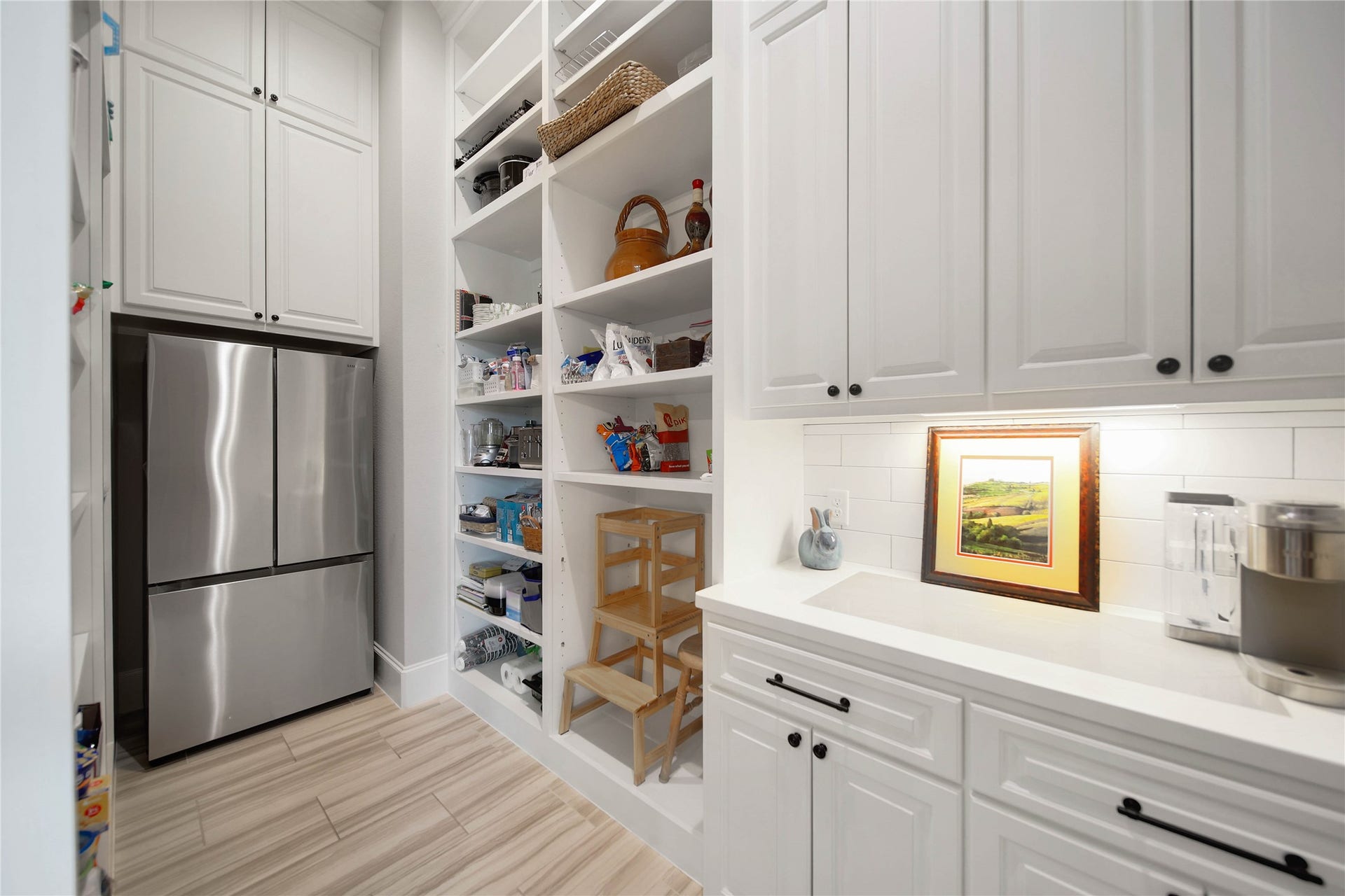 24718 Shadow Pond Drive, Spring, TX 77389 Elegant pantry featuring ample storage with sleek white cabinetry, a modern stainless steel refrigerator, and illuminated counter space perfect for organizing essentials.