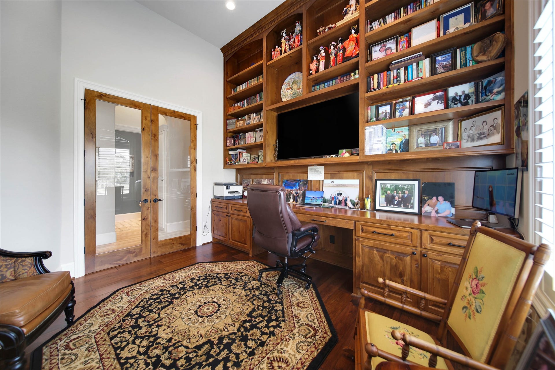 24718 Shadow Pond Drive, Spring, TX 77389 Elegant home office featuring custom wood built-in shelving, a spacious desk, and French doors, complemented by rich hardwood flooring and abundant natural light.