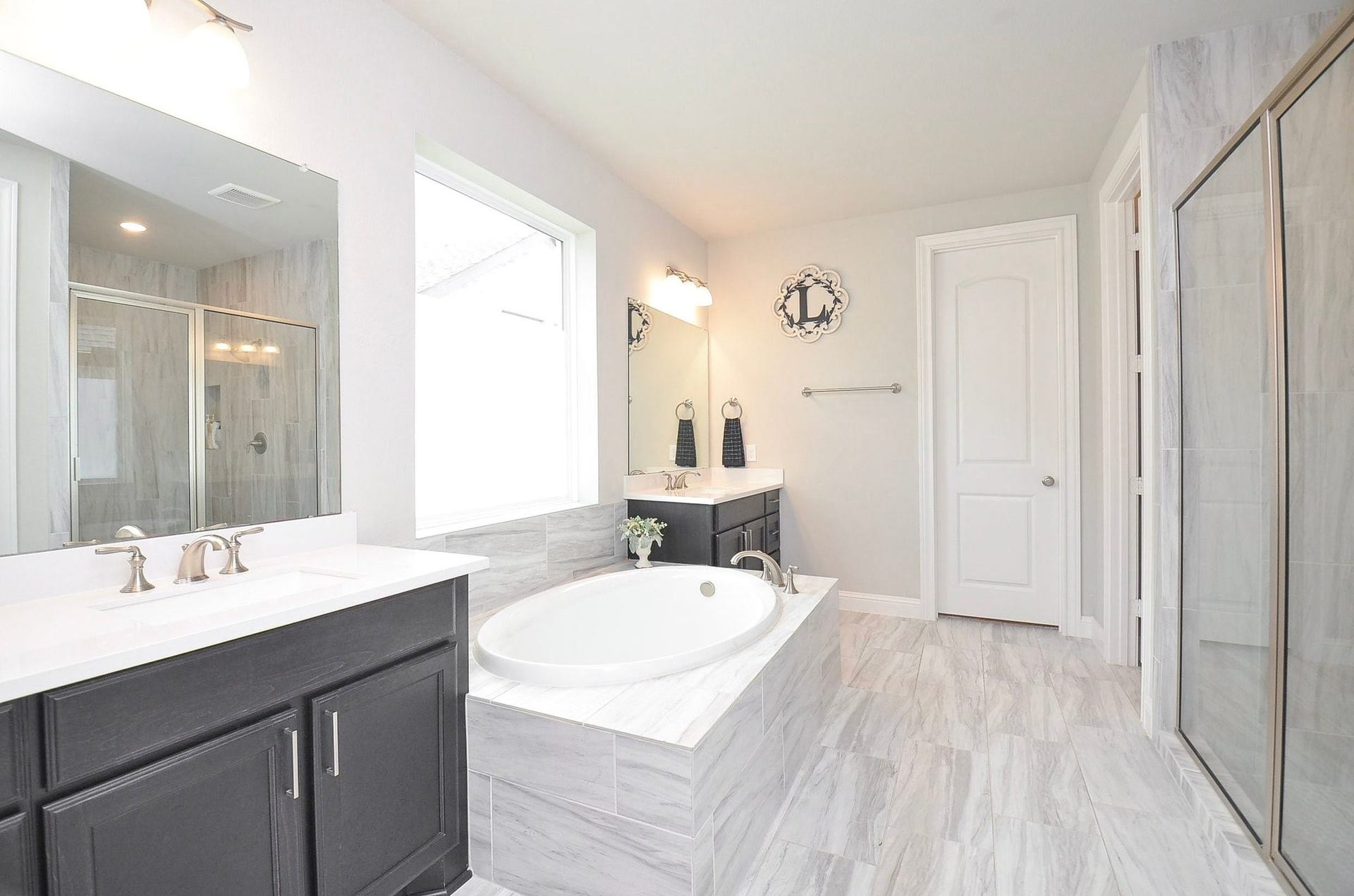 Indulge in a little everyday luxury in your spacious 15' x 15' spa-inspired primary bathroom, featuring separate vanities, a soaking tub beneath a large window, and an oversized walk-in shower.