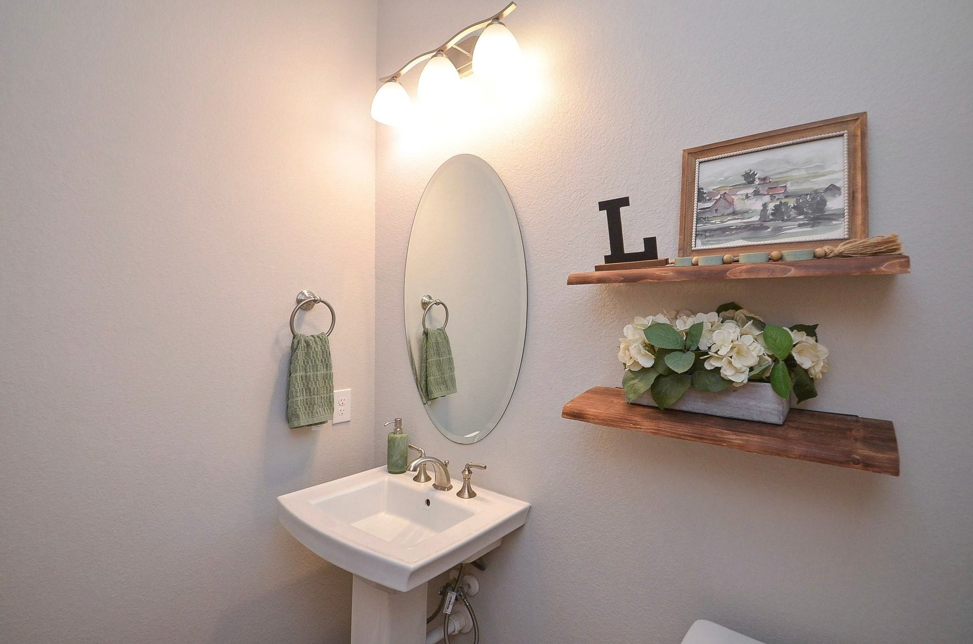 Your convenient 6' x 4' first-floor powder room offers a welcoming space for guests, featuring a classic pedestal sink, elegant mirror, and decorative shelving.