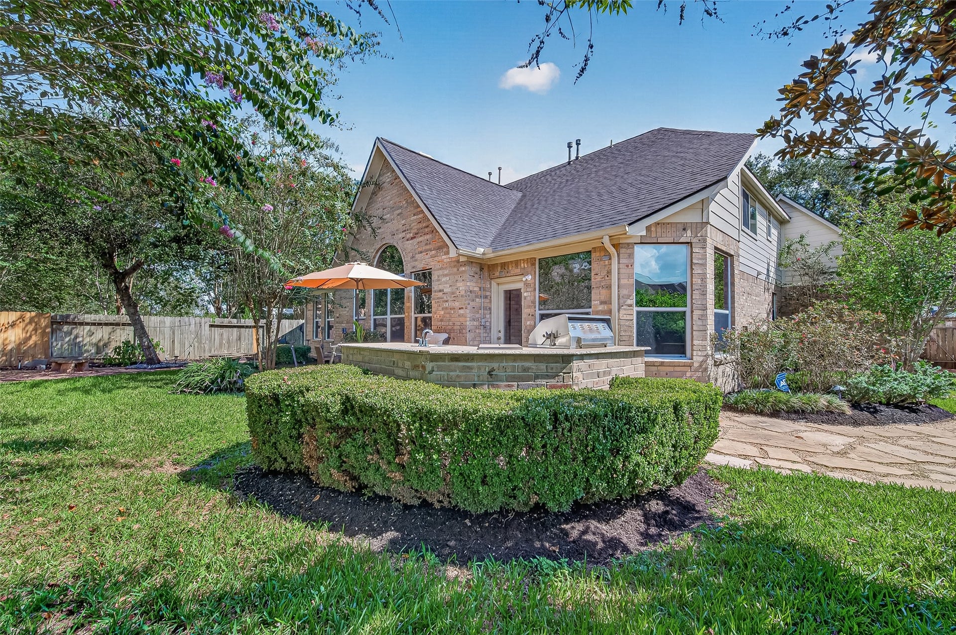 13611 Cottage Arbor Court, Sugar Land, TX 77498 Beautifully landscaped backyard offering mature trees, lush green space, and a spacious patio with built-in outdoor kitchen; an inviting setting for relaxing and entertaining.