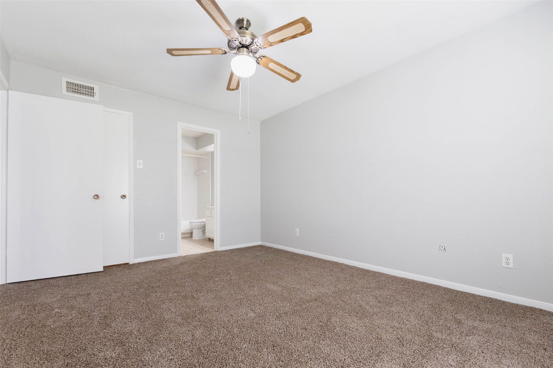 Spacious carpeted bedroom featuring neutral paint, ceiling fan, and convenient access to the adjoining bathroom.