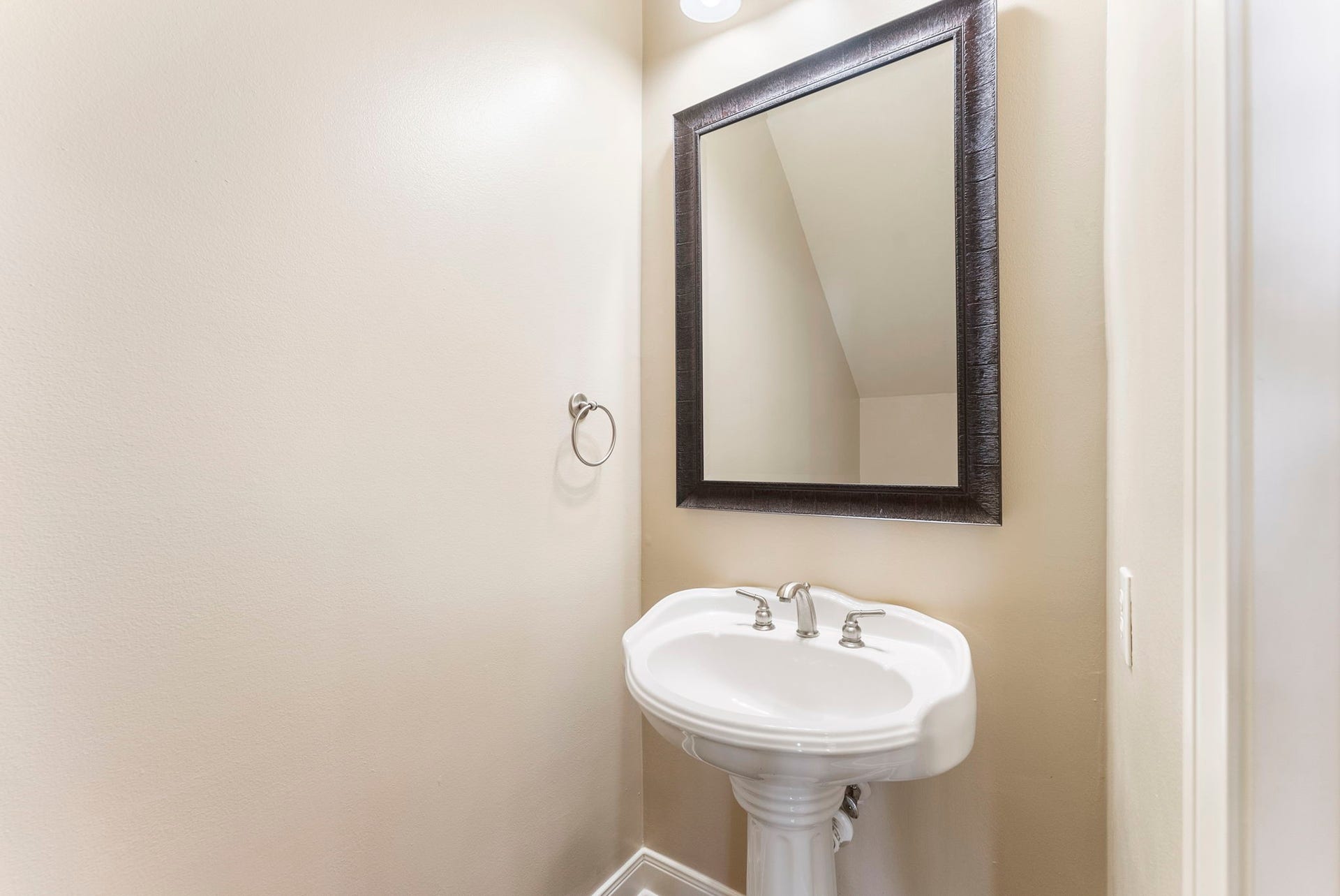 24 Riva Row, Spring, TX 77380 A convenient main-level powder room with a classic pedestal sink and framed mirror, perfect for guests.