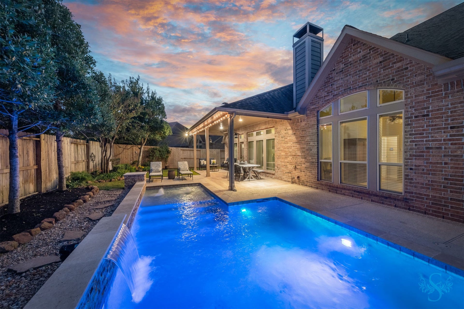 5219 Kenton Place Lane, Fulshear, TX 77441 Brilliant blue pool lighting and a cascading waterfall transform the backyard into an enchanting evening escape. Enjoy a refreshing swim before unwinding beneath the covered patio, surrounded by lush landscaping and the soothing sound of water.