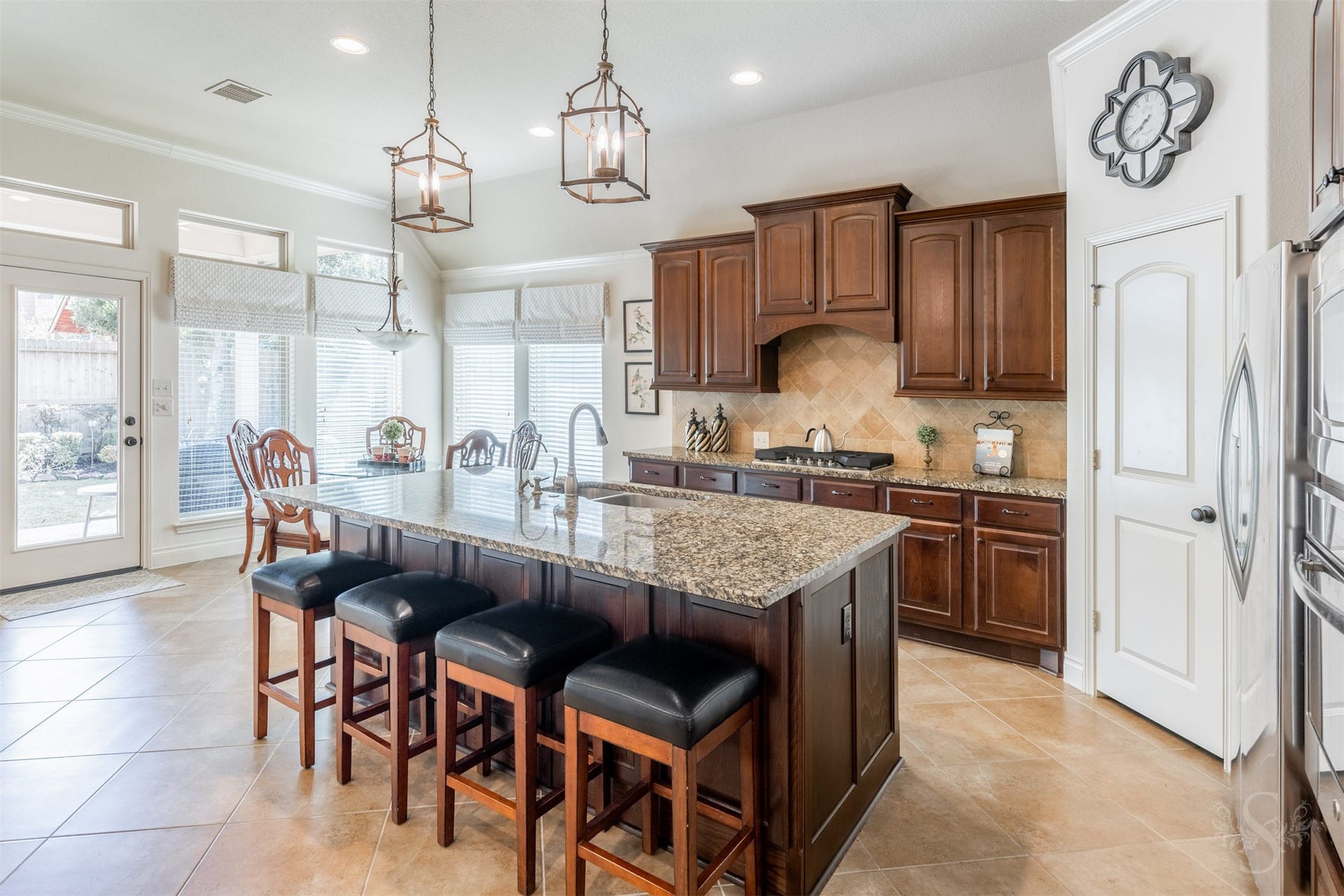5219 Kenton Place Lane, Fulshear, TX 77441 The beautifully appointed kitchen pairs an expansive granite island with rich raised panel cabinetry and a gas cooktop. Breakfast bar seating and the adjoining breakfast room offer inviting places to gather, with tall windows framing views of the backyard.