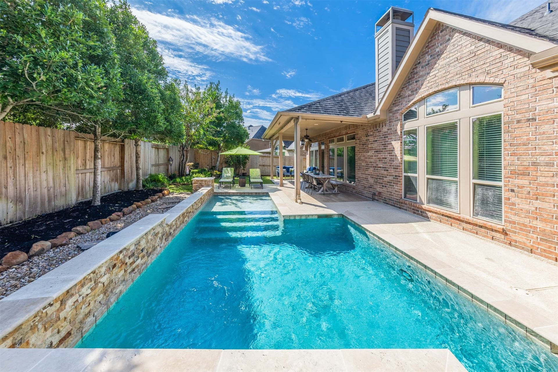 5219 Kenton Place Lane, Fulshear, TX 77441 Spend sun-filled afternoons swimming and relaxing in the sparkling pool, beautifully framed by a raised stone wall and lush landscaping. The covered patio offers a welcoming place for poolside dining and leisurely conversation in this exquisite backyard retreat.
