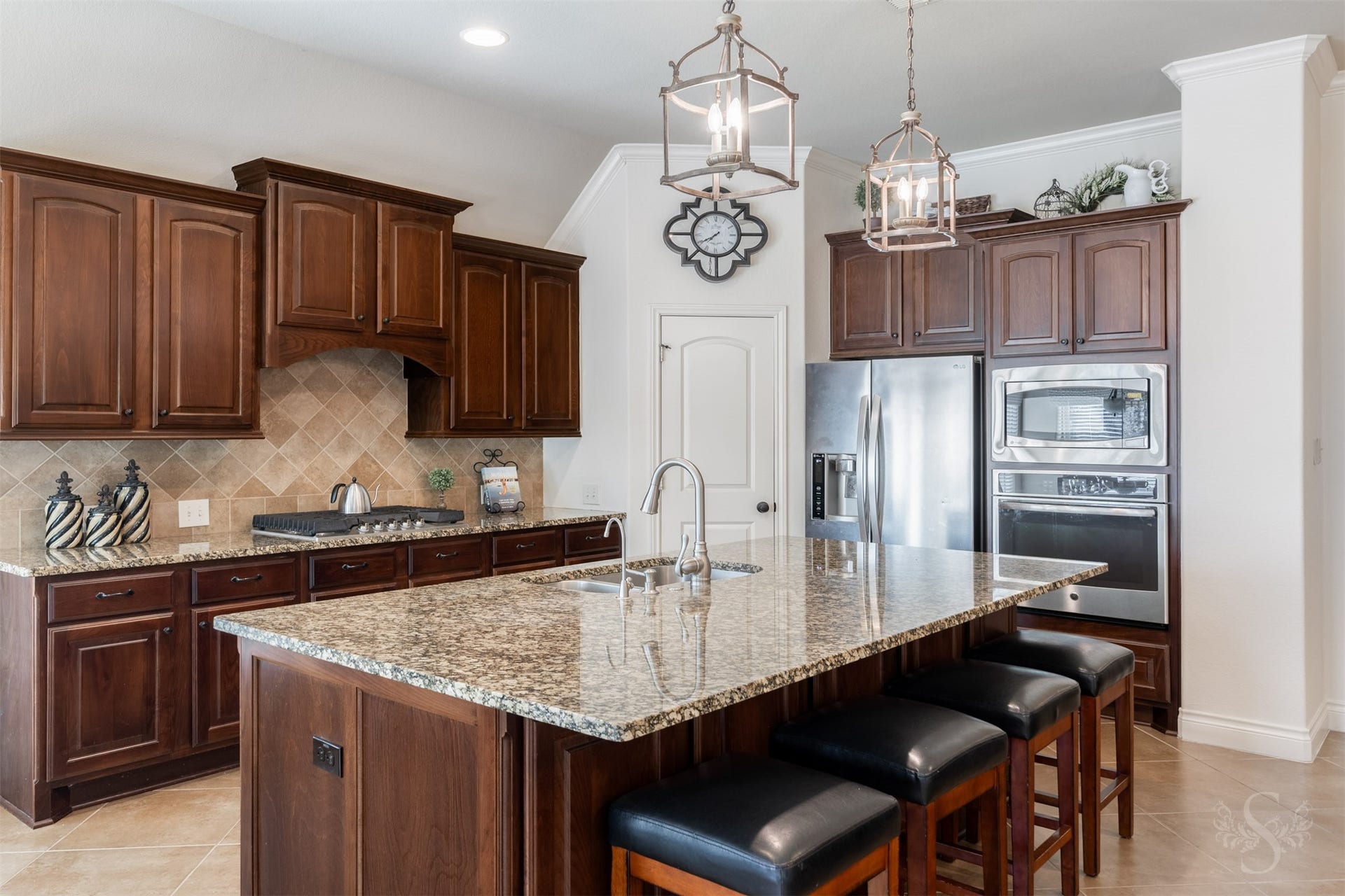 5219 Kenton Place Lane, Fulshear, TX 77441 An expansive granite island with breakfast bar seating takes center stage beneath a pair of elegant lantern pendants. Richly stained 42-inch raised panel cabinetry, a diagonal tile backsplash and built-in stainless steel oven and microwave give the kitchen its timeless appeal.