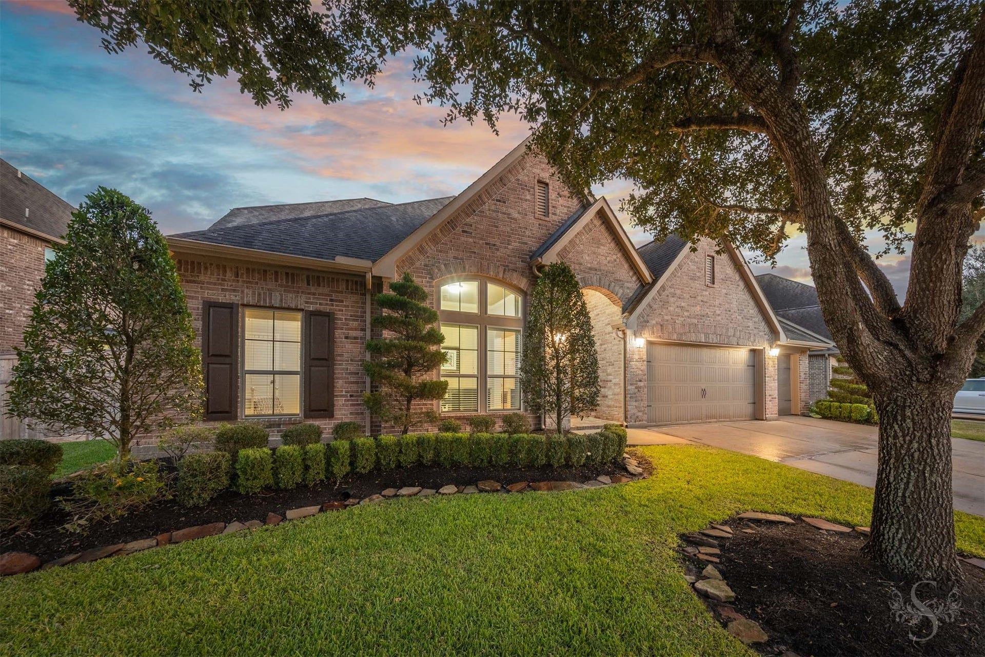 5219 Kenton Place Lane, Fulshear, TX 77441 Warm evening illumination highlights the intricate brickwork, graceful gables and impressive arched entrance. Sculpted topiaries and beautifully bordered landscaping complement the homes timeless elegance.