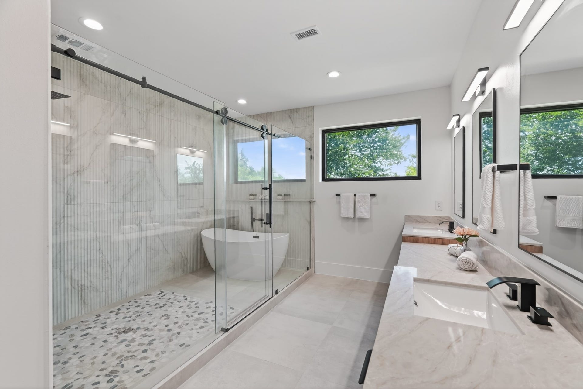 Spa-inspired primary bathroom with his-and-hers vanities, a dedicated makeup station, a large walk-in shower, a separate soaking tub, and beautiful natural light.