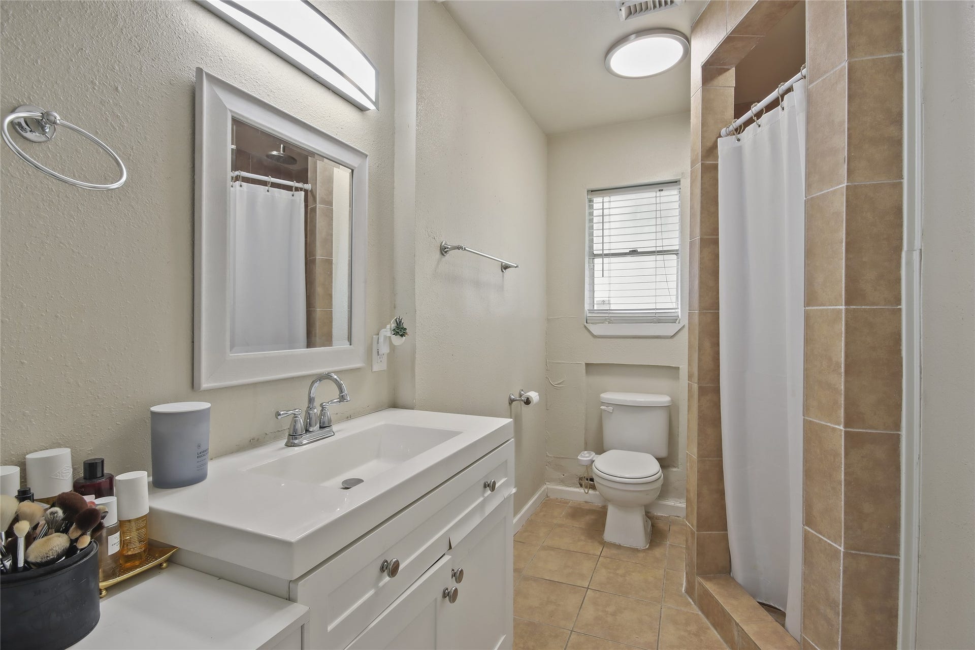 910 Centerwood Drive, Houston, TX 77013 The primary bathroom features a tiled walk-in shower with a rainfall showerhead, a wide vanity with generous counter space, and a window that brings in natural light.