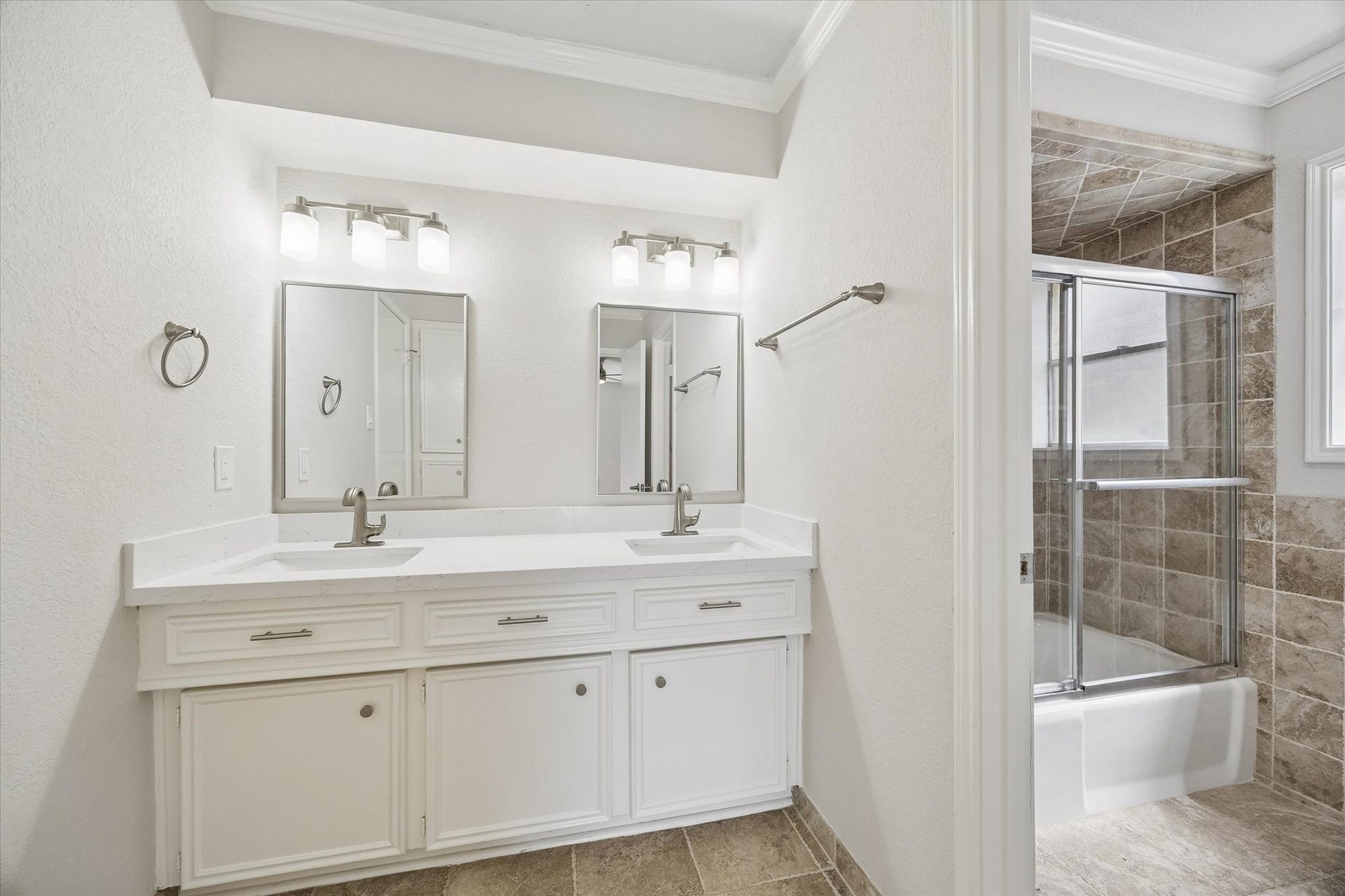 3122 Peach Tree Lane, Missouri City, TX 77459 This bathroom features a modern double vanity with sleek fixtures, ample lighting, and a large mirror. It includes a tiled shower-tub combination with glass doors, providing a clean and contemporary look.