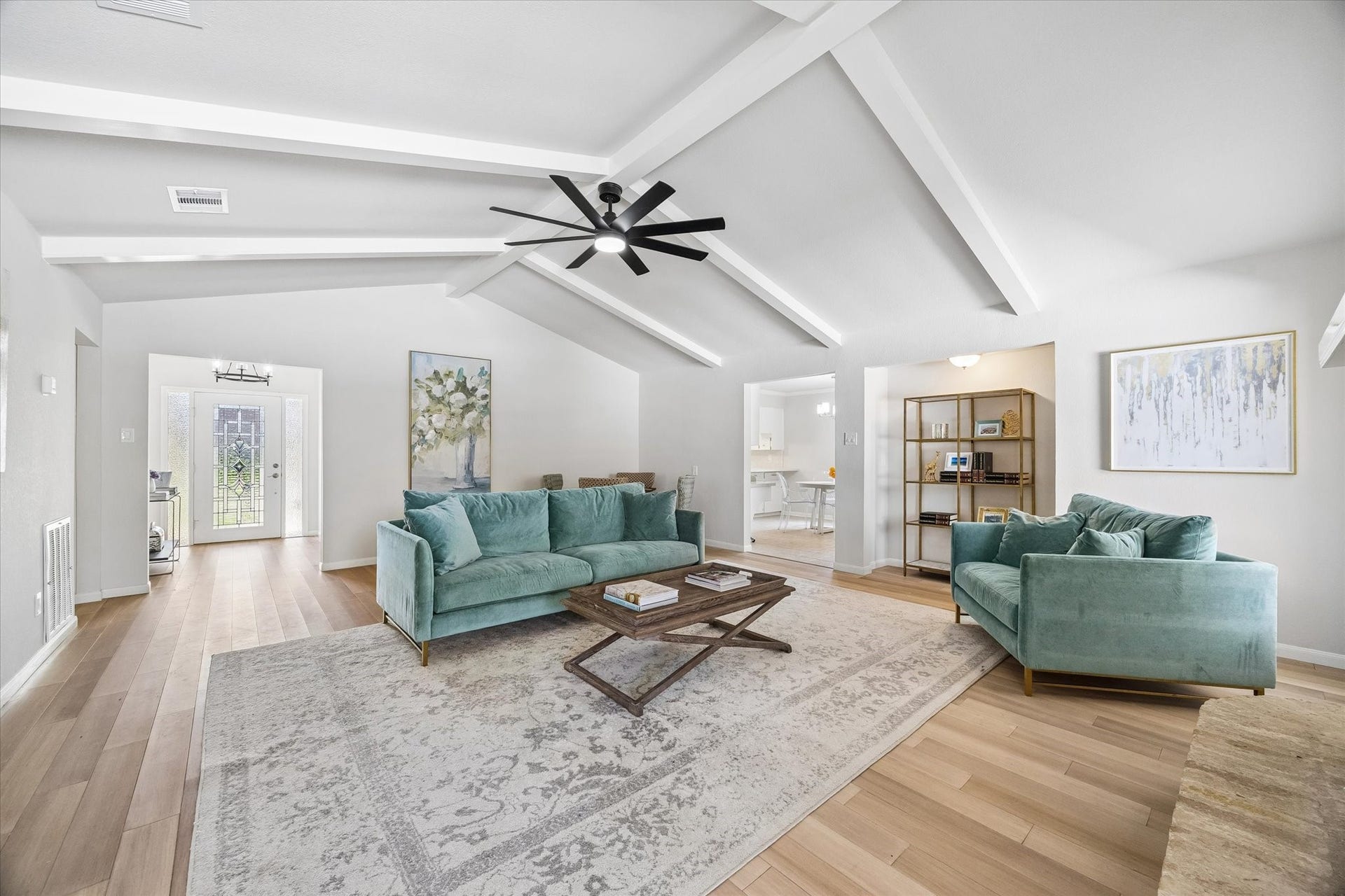 3122 Peach Tree Lane, Missouri City, TX 77459 This photo showcases a spacious, bright living room with high vaulted ceilings and exposed beams. It features modern light fixtures, hardwood floors, and elegant furnishings. Large windows and a neutral color palette enhance the airy, inviting atmosphere.