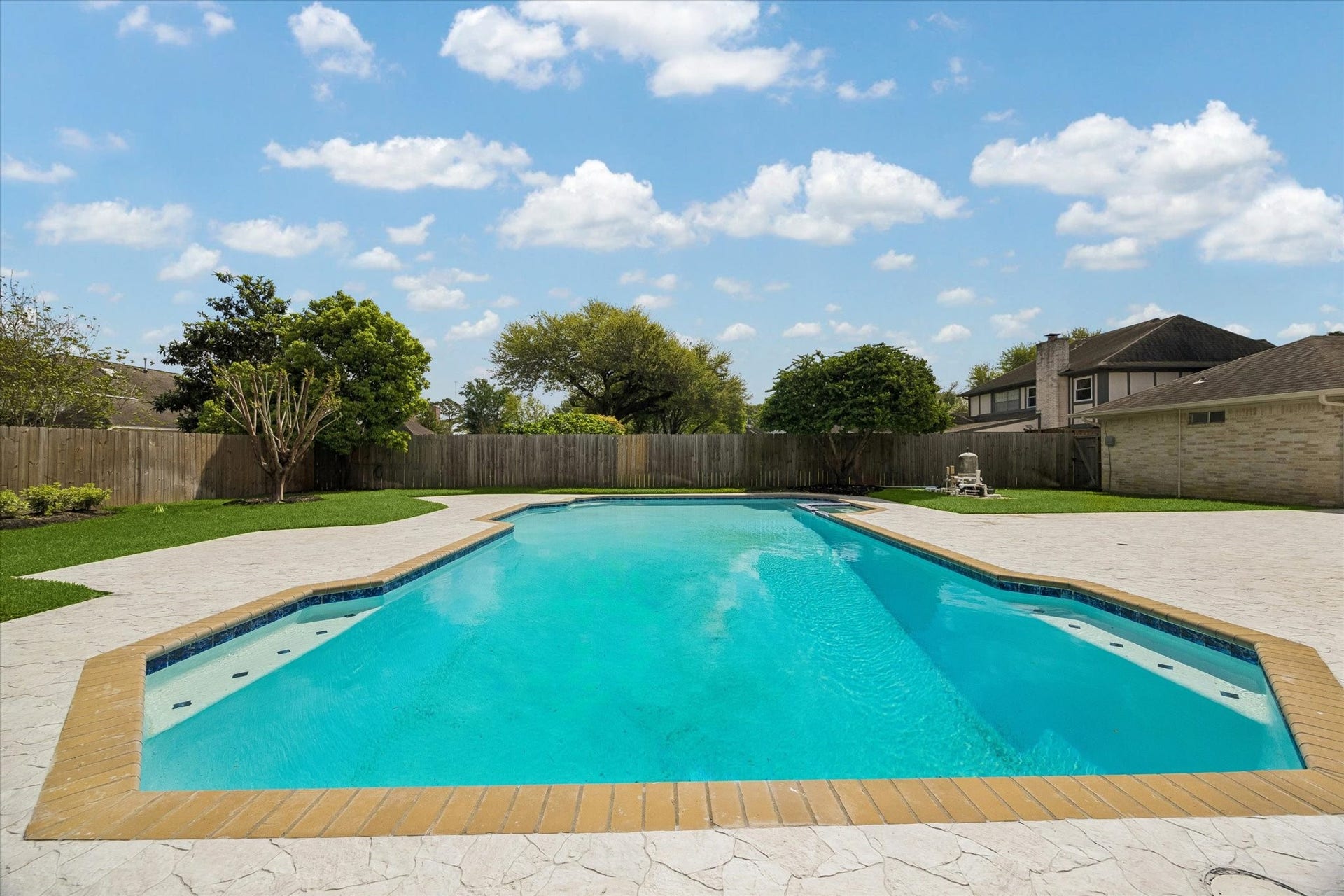 3122 Peach Tree Lane, Missouri City, TX 77459 This photo showcases a spacious backyard with a large, inviting swimming pool surrounded by a concrete deck. The area is enclosed by a wooden fence and features well-maintained landscaping with mature trees, offering a private and serene outdoor space.