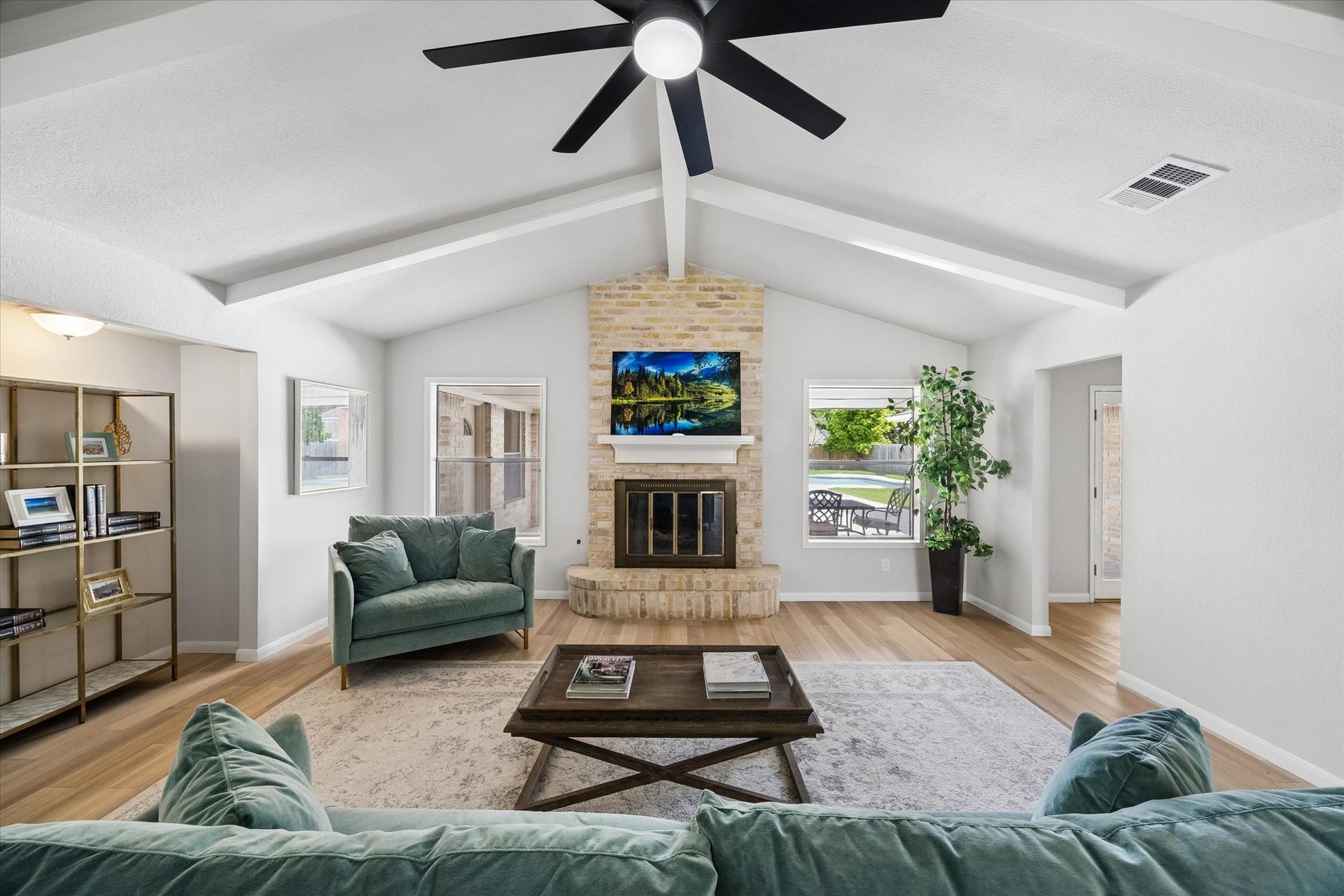 3122 Peach Tree Lane, Missouri City, TX 77459 This spacious living room features a vaulted ceiling with a modern fan, a cozy brick fireplace, and abundant natural light from multiple windows. Perfect for relaxation and entertaining.