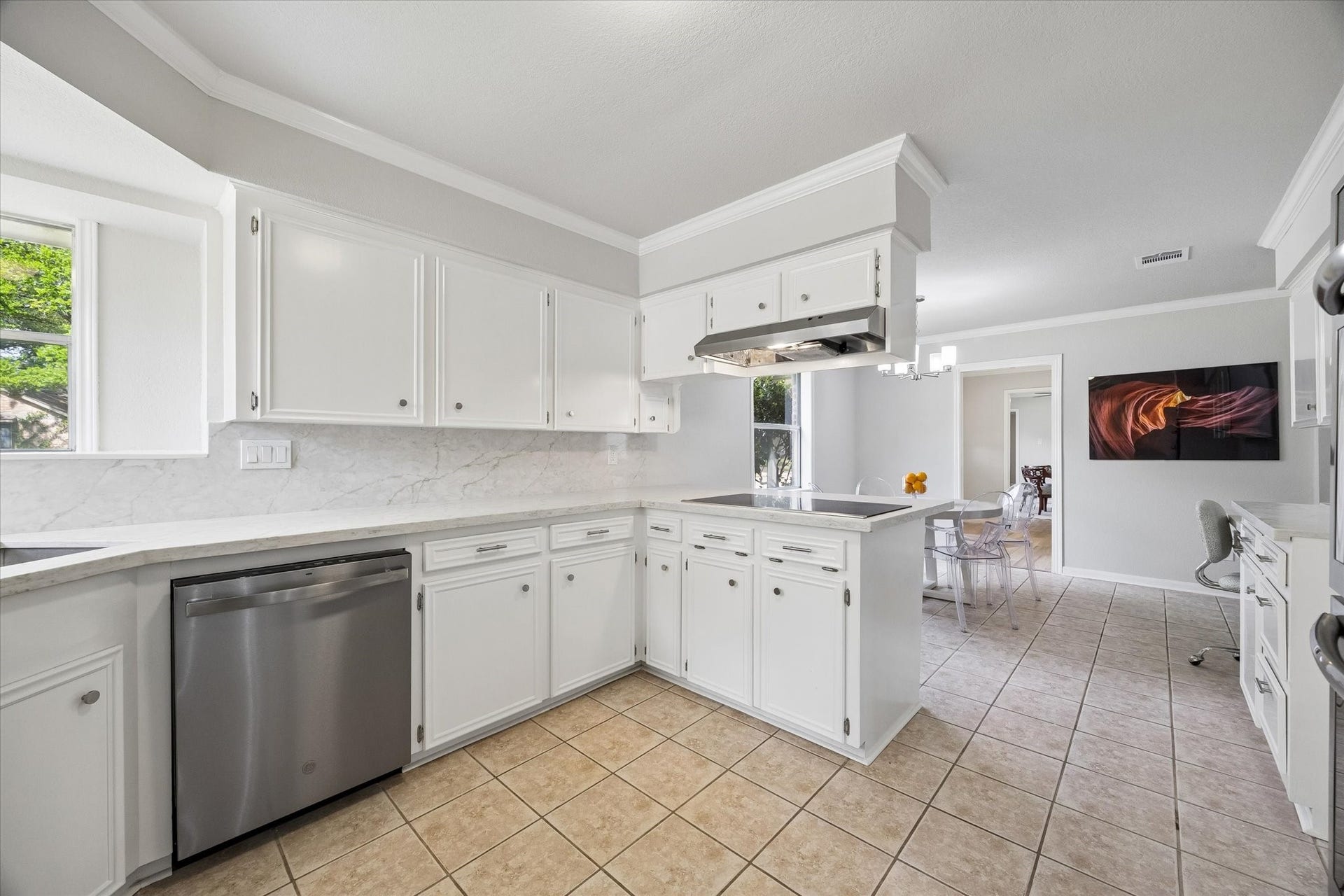 3122 Peach Tree Lane, Missouri City, TX 77459 This kitchen features bright white cabinetry, a sleek stainless-steel dishwasher, and a stylish tile floor. It opens to a breakfast area with ample natural light, creating an inviting space for cooking and entertaining.
