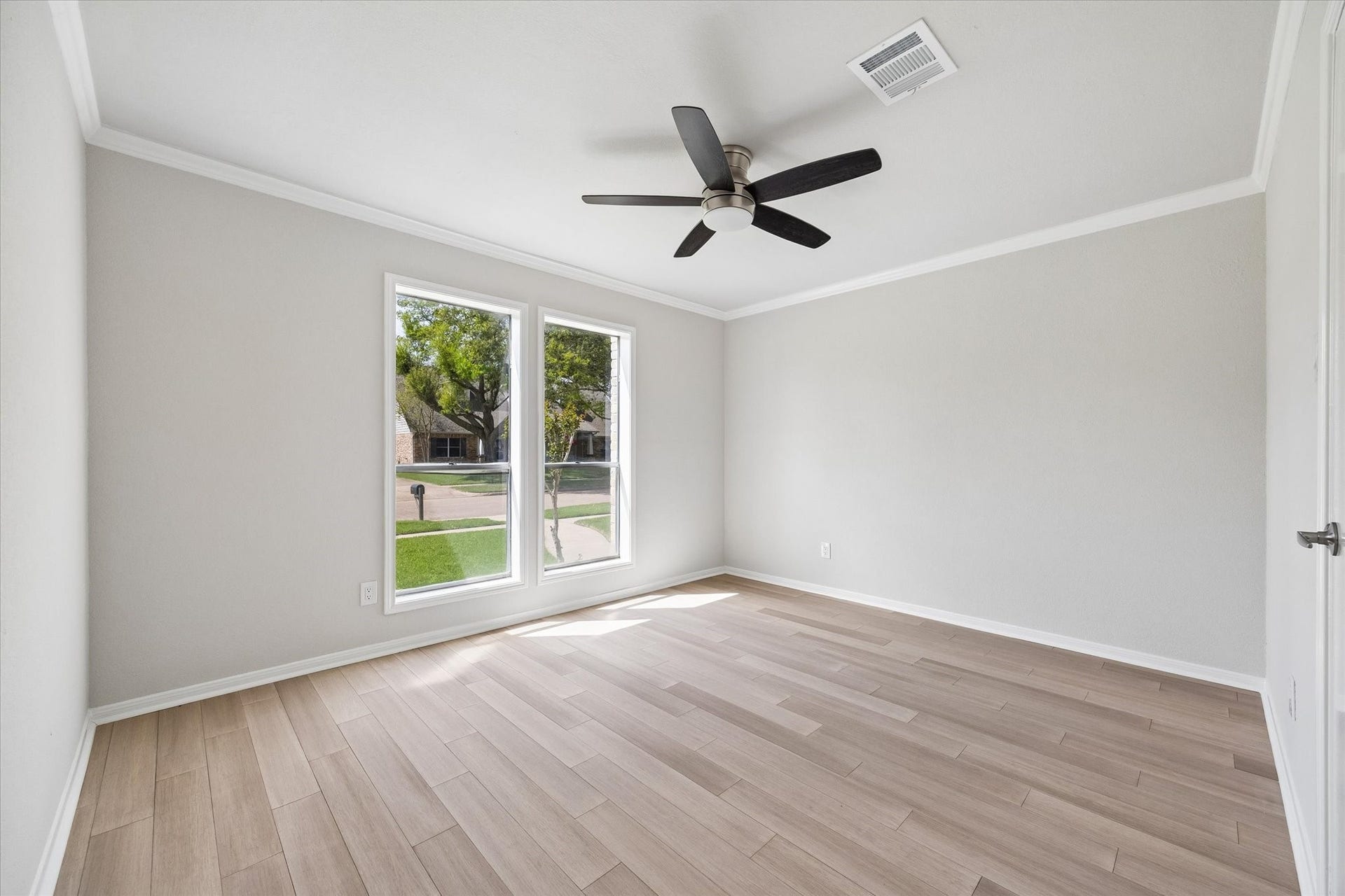 3122 Peach Tree Lane, Missouri City, TX 77459 A bright, minimalist bedroom featuring light wood flooring, neutral walls, and a modern ceiling fan. Large windows provide ample natural light and a view of the street.