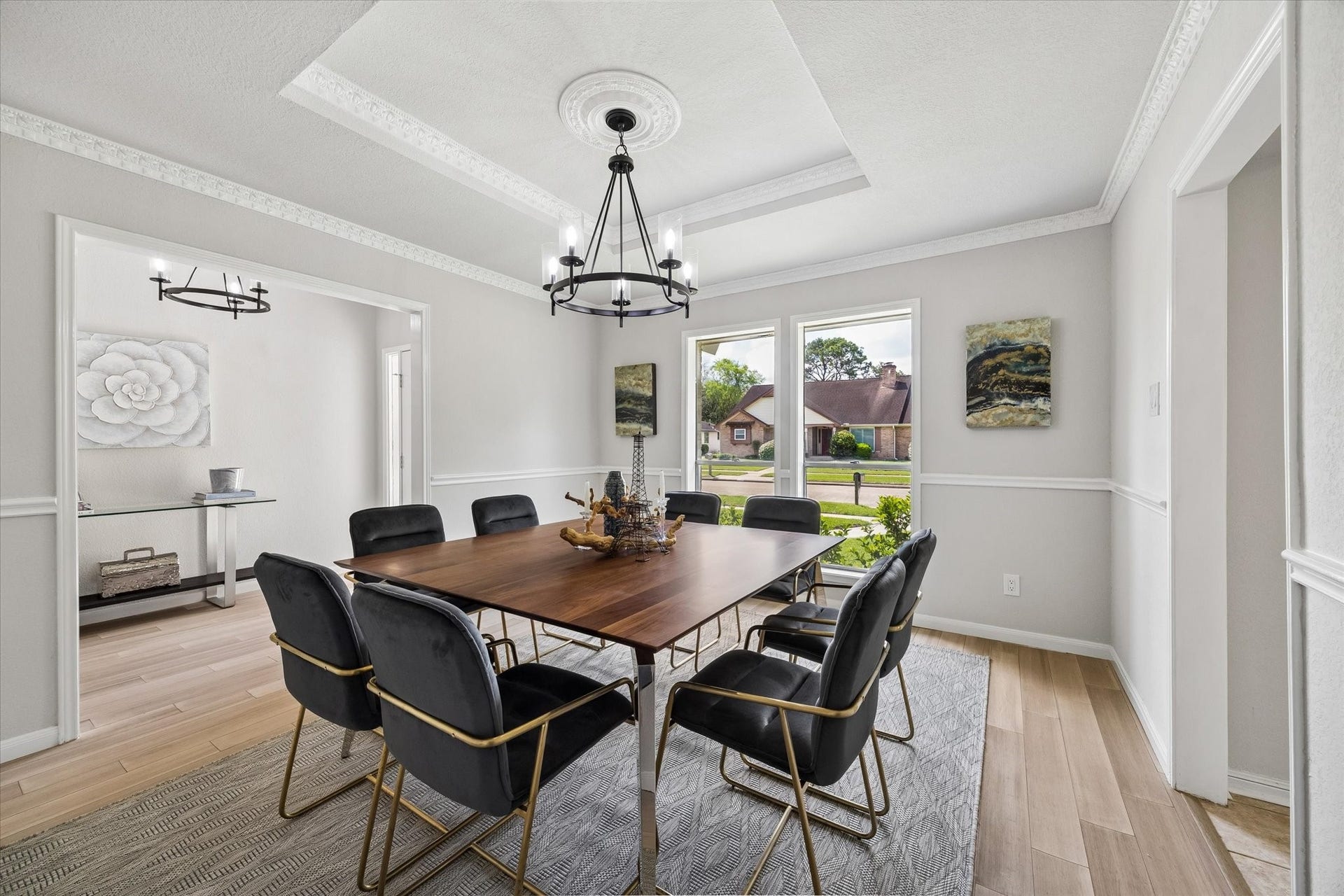 3122 Peach Tree Lane, Missouri City, TX 77459 This dining room features a modern chandelier, a large wooden table with stylish black chairs, and ample natural light from three windows. The neutral walls and decorative molding create an elegant and inviting atmosphere, perfect for entertaining.
