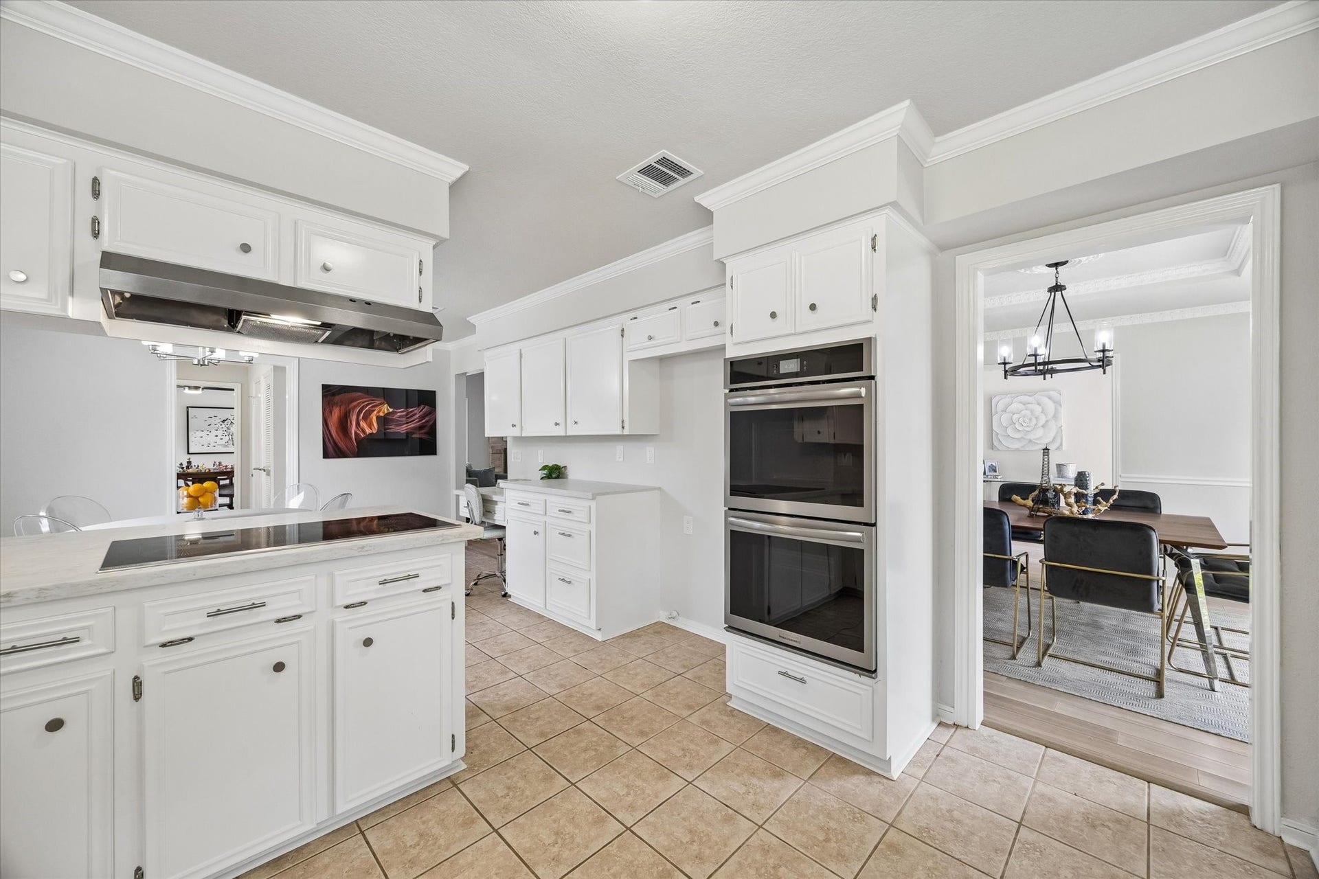 3122 Peach Tree Lane, Missouri City, TX 77459 This photo showcases a bright, spacious kitchen with white cabinetry, a modern cooktop, and double ovens. The tile flooring complements the clean aesthetic, and there's a seamless flow into a stylish dining area with elegant lighting.