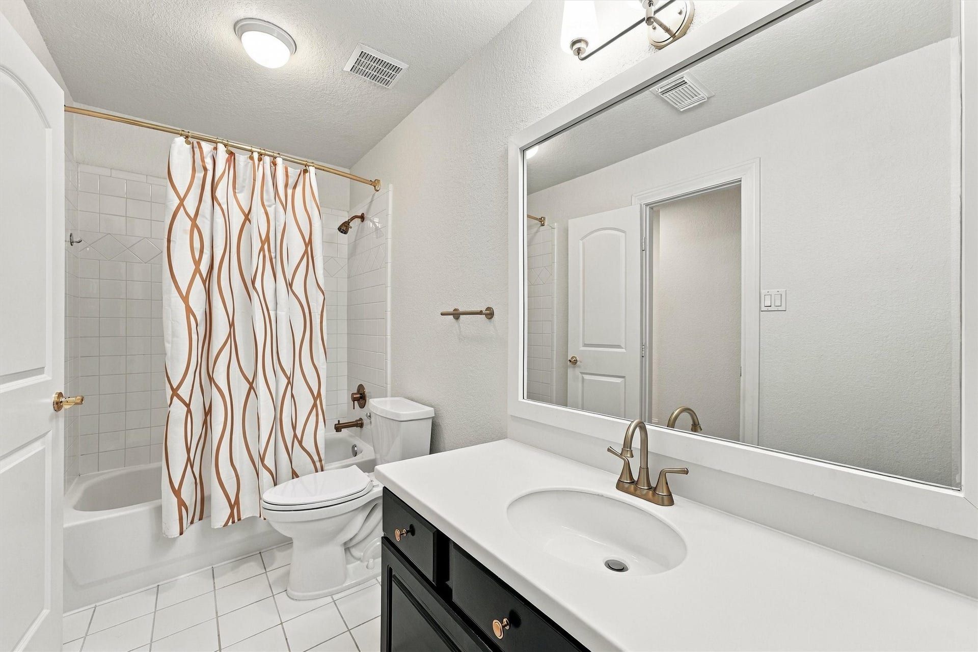22415 Elizabeth Place Court, Katy, TX 77494 Second floor - Second Bathroom with black vanity, large framed mirror, brass fixtures, white tile floor, and a tub and shower combination with tile surround.