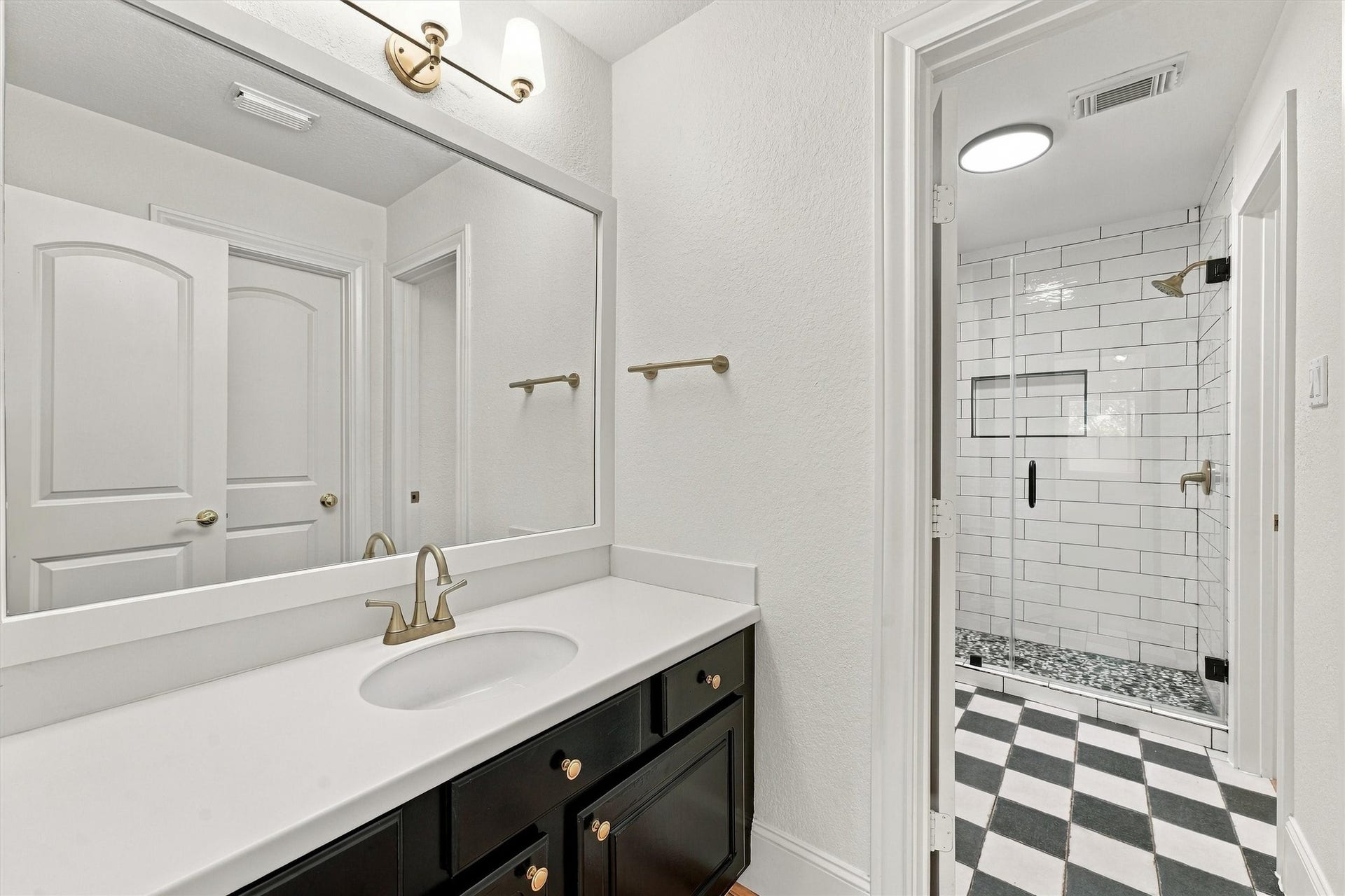 22415 Elizabeth Place Court, Katy, TX 77494 Second floor - Third Bathroom with black vanity, large framed mirror, brass fixtures, checkerboard tile floor, and a walk-in shower with white subway tile, niche, and glass door.