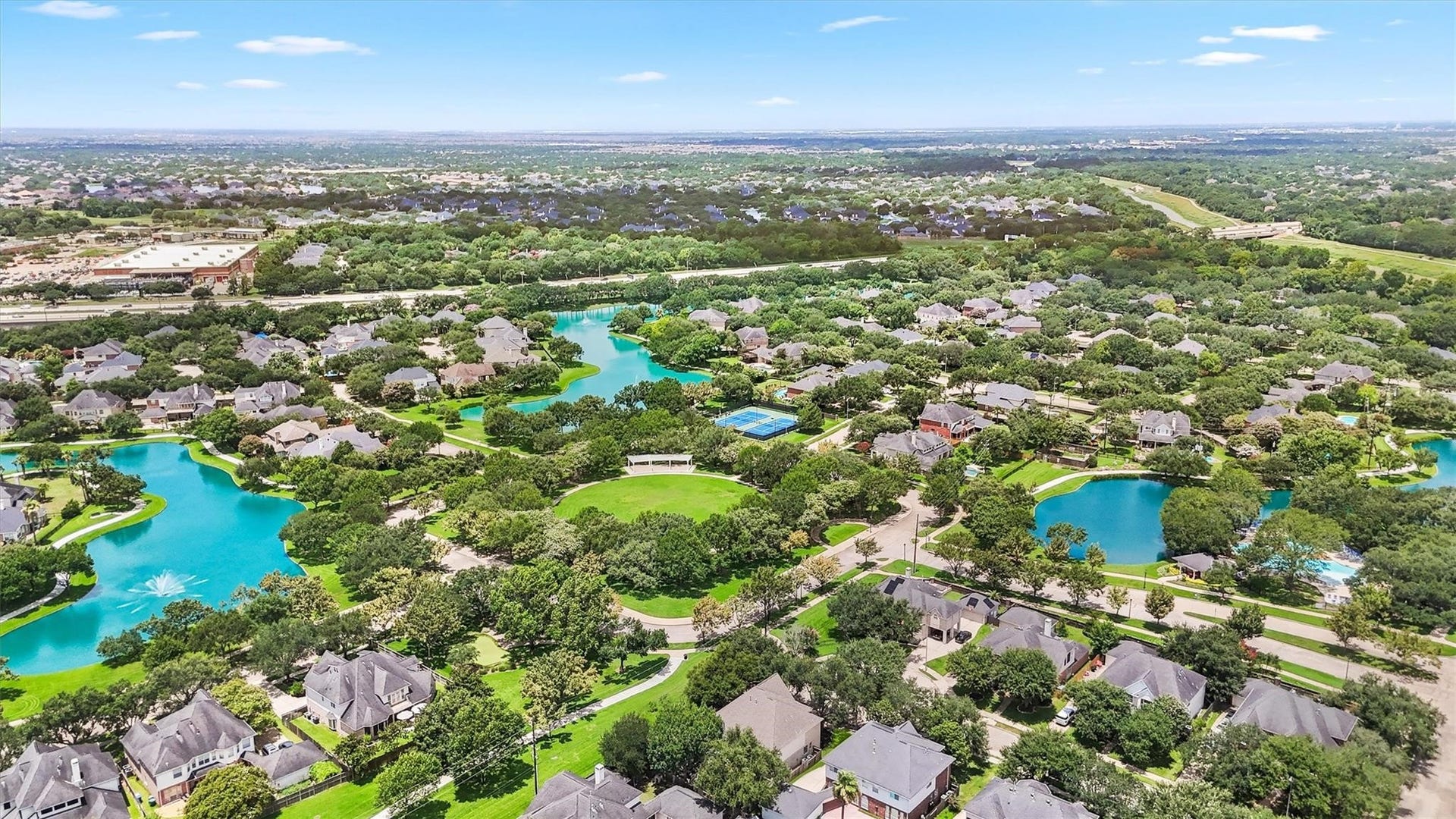22415 Elizabeth Place Court, Katy, TX 77494 This aerial photo showcases a pictures que Grand Lakes neighborhood with lush greenery, winding streets, and houses nestled around serene blue lakes. The area features ample green space and a community pool.