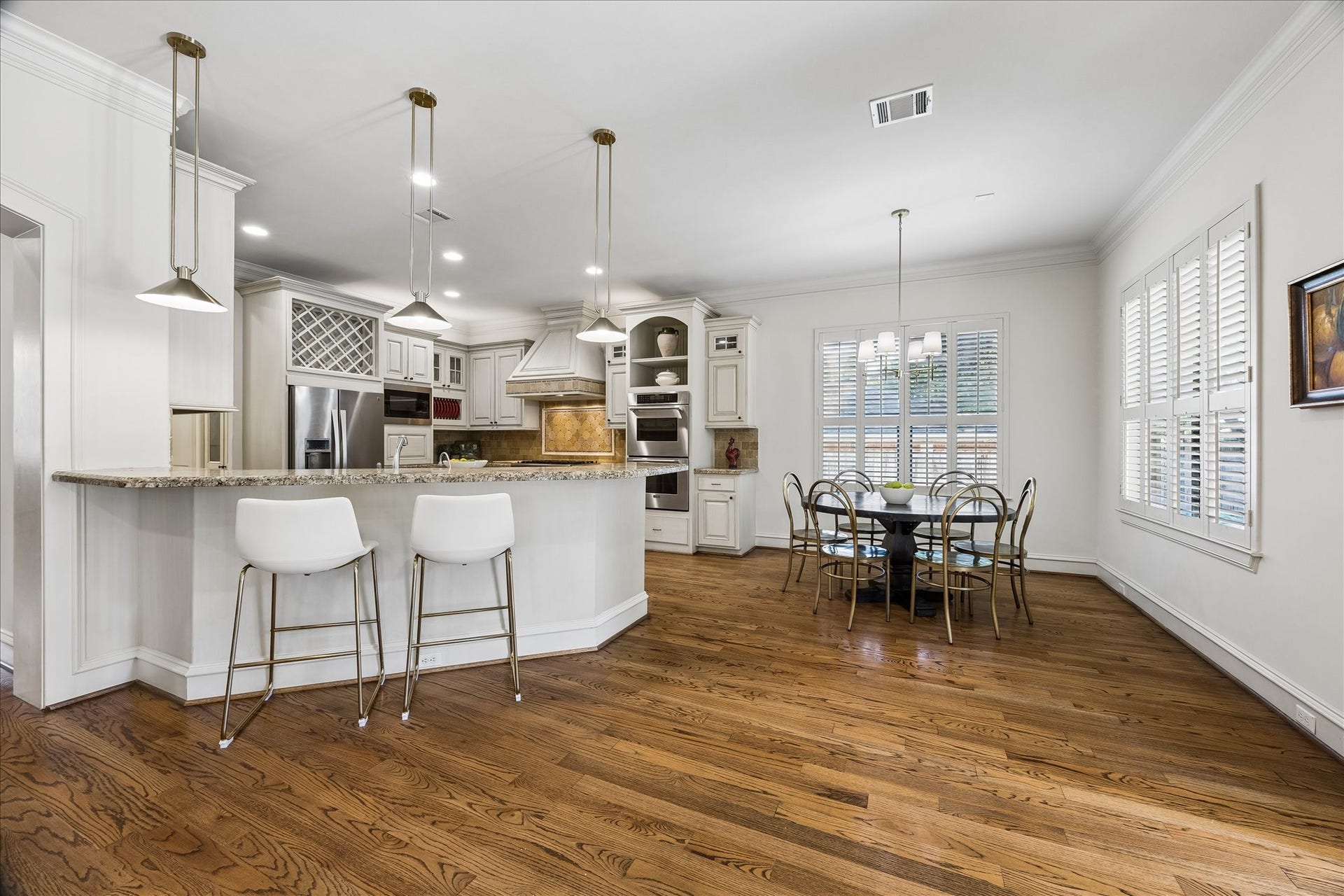 4037 Dumbarton Street, Houston, TX 77025 Spacious kitchen with hardwood floors, features a large island with bar seating, stainless steel appliances, and a large breakfast area with ample natural light from the shuttered windows.
