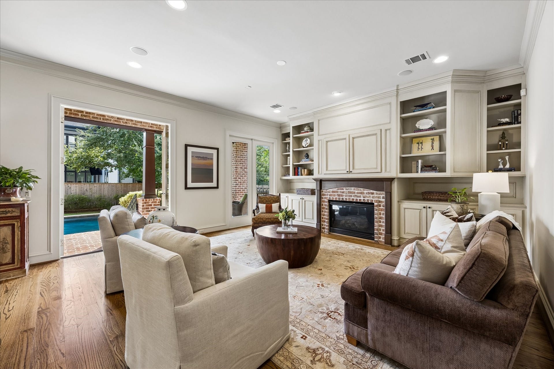 4037 Dumbarton Street, Houston, TX 77025 Warm and welcoming family room with built-in shelving, a cozy fireplace, and large windows that open to a serene patio and pool area, offering seamless indoor-outdoor living.