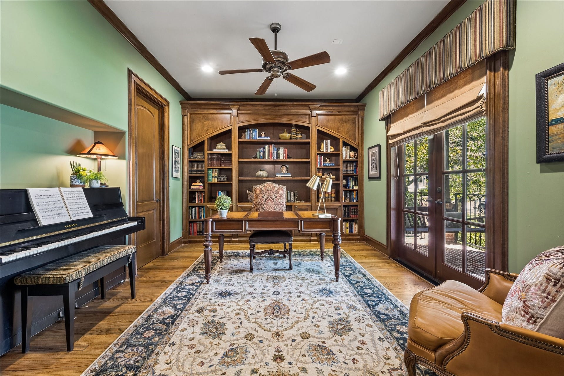 4037 Dumbarton Street, Houston, TX 77025 Elegant home office featuring built-in wooden bookshelves and French doors opens to a serene outdoor view, complemented by warm wood accents.