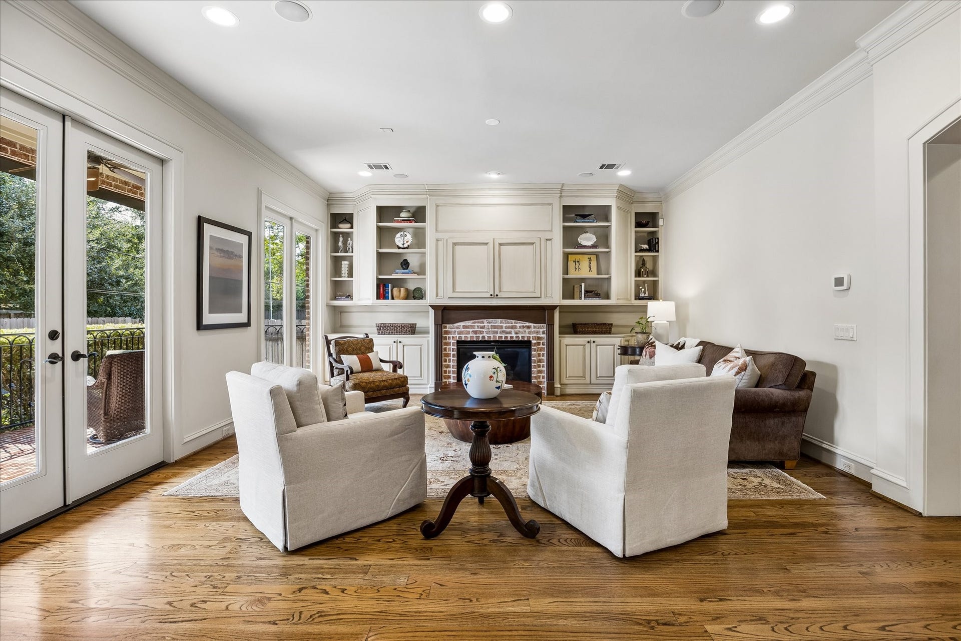 4037 Dumbarton Street, Houston, TX 77025 Inviting family room with hardwood floors, features a cozy fireplace flanked by built-in shelves. Ample natural light streams through French doors, opening to a serene outdoor space.