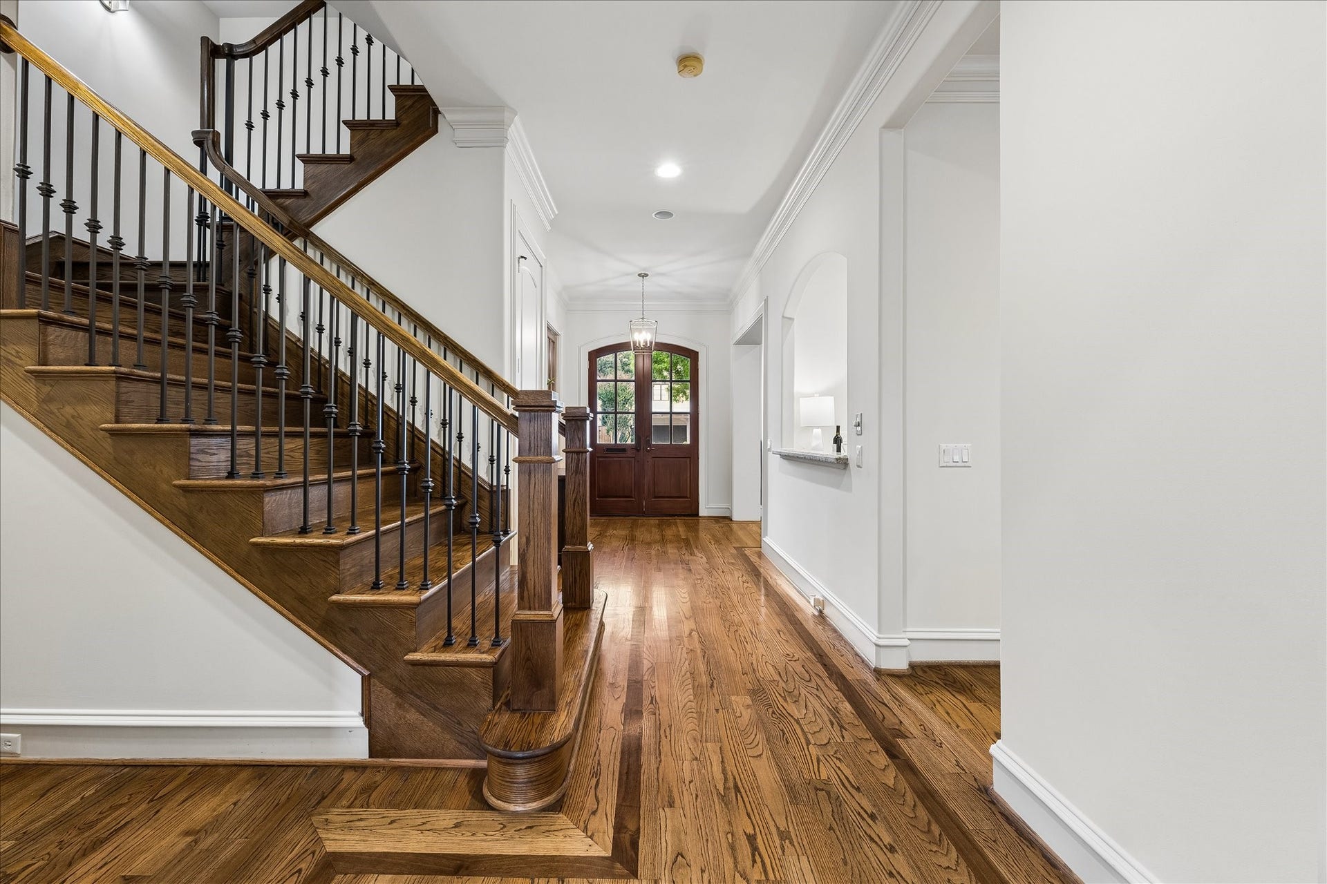 4037 Dumbarton Street, Houston, TX 77025 Elegant entryway featuring rich hardwood floors and a striking staircase with classic iron balusters, leads to a welcoming doorway that enhances the home's inviting ambiance.