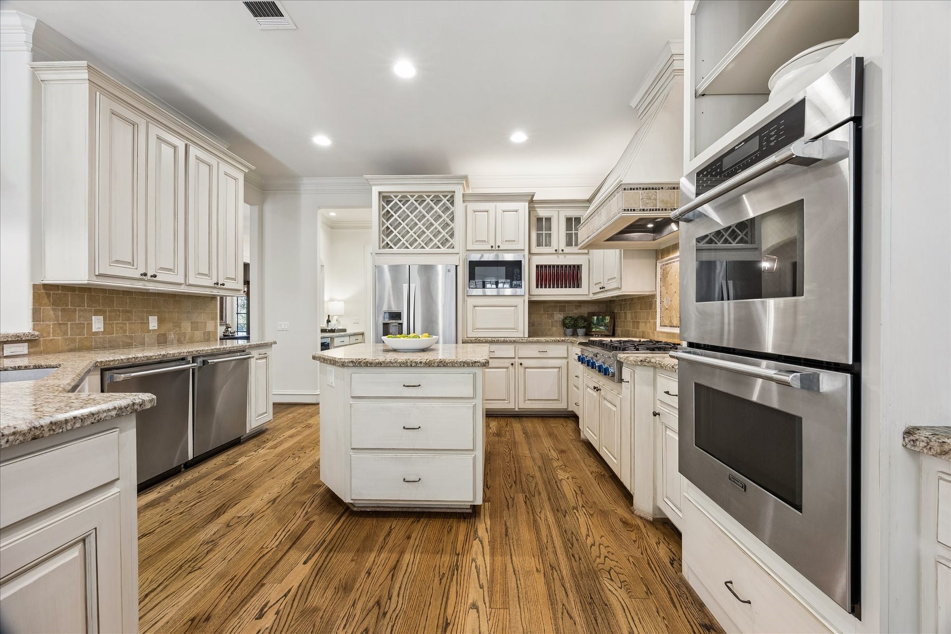 4037 Dumbarton Street, Houston, TX 77025 A true cook's kitchen featuring stainless steel appliances, expansive countertops, and custom cabinetry, enhanced by a spacious island and warm hardwood floors.