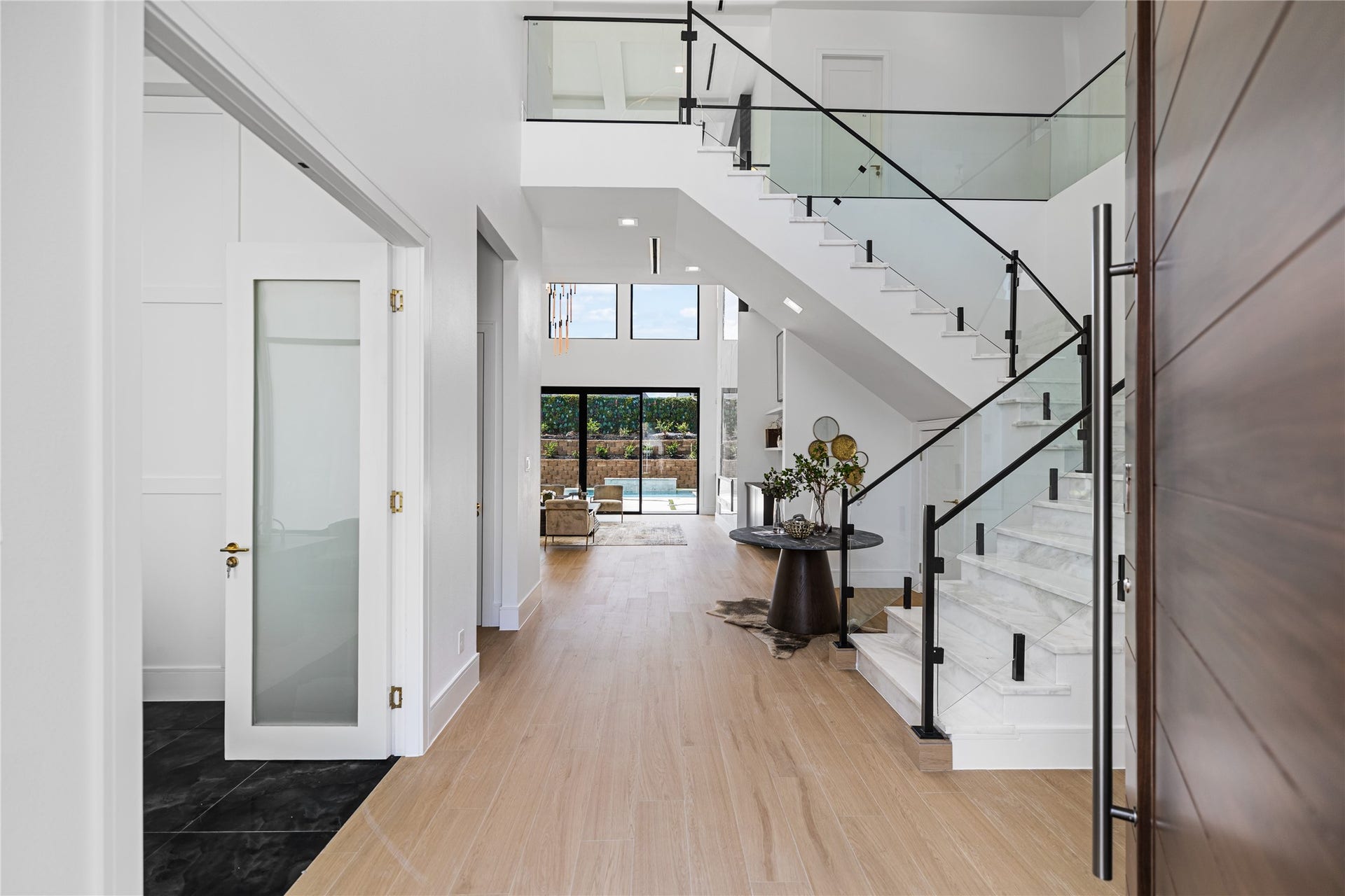 A two-story sweeping foyer welcomes you inside this impressive pivot front door. A first-floor private office/study is to the left., An ensuite guest quarters is to the right through a hallway. A soaring glass and iron staircase and white oak floors lead you straight into the heart of the home.
