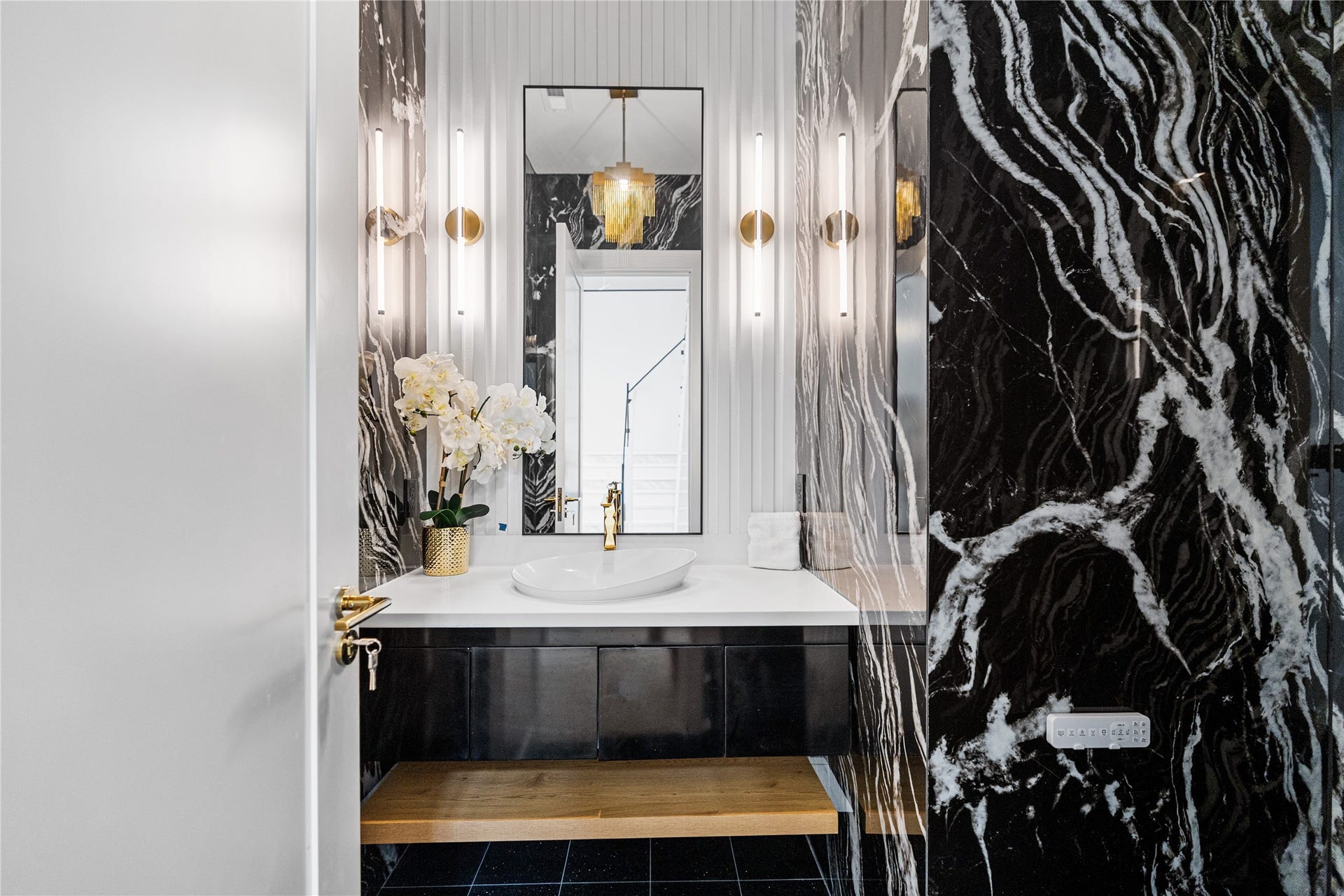 A dramatic and sophisticated first-floor powder bath featuring luxurious finishes and striking custom lighting. Powder bath is located in the foyer adjacent to the office.