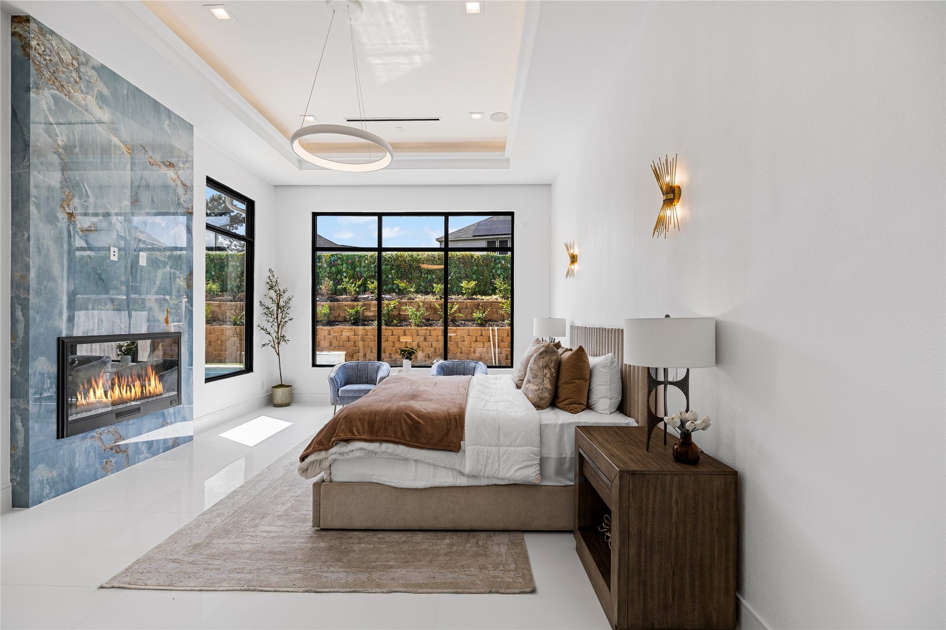 Welcome inside your extraordinary private sanctuary. The expansive primary suite is framed by oversized windows overlooking your secluded backyard oasis, while a striking custom marble fireplace extends dramatically from floor to ceiling. Soft, ambient ceiling details complete the space, creating an atmosphere of warmth, elegance, and effortless tranquility.
