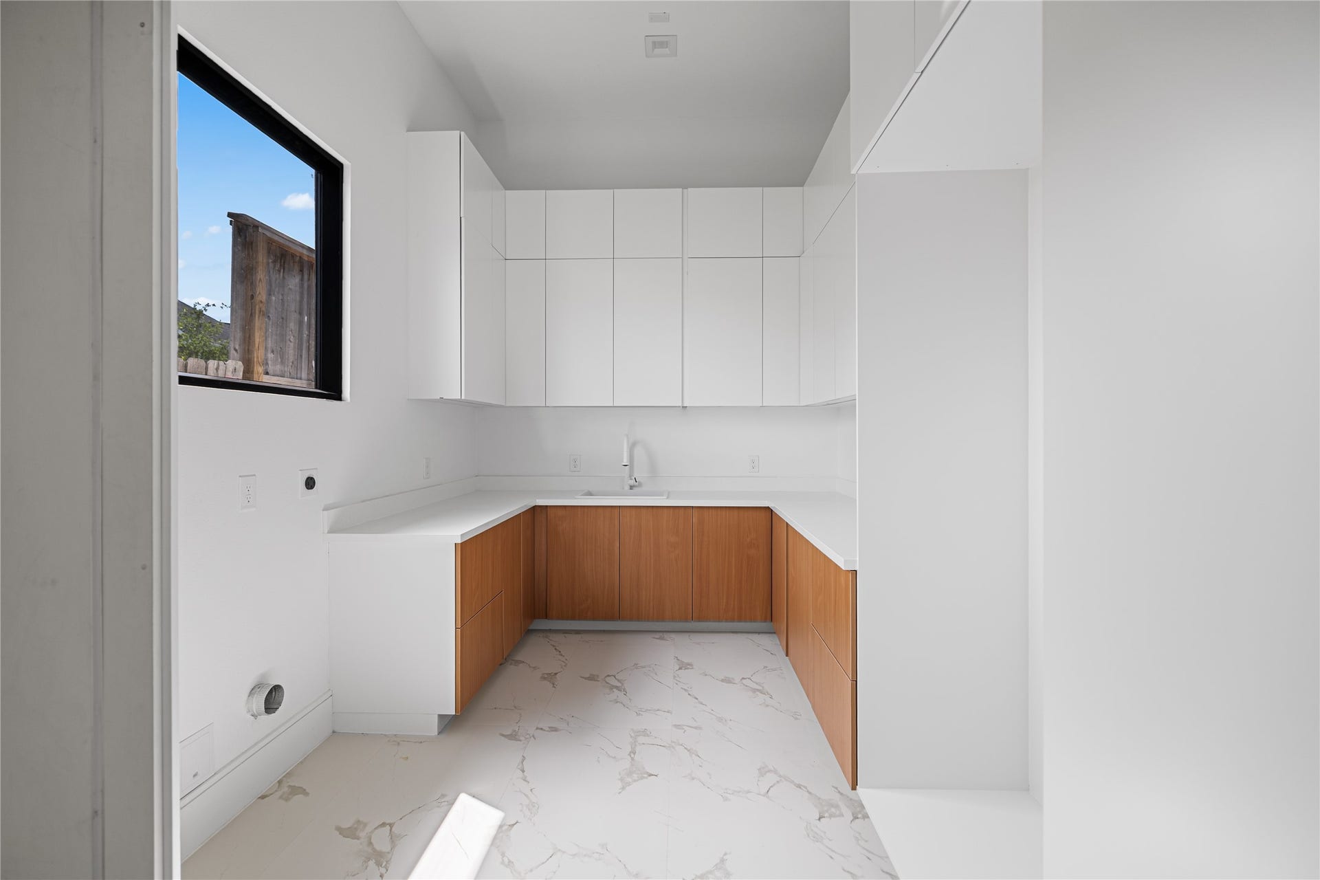 A generously-sized first-floor utility room tucked away discreetly across the hall from the walk-in pantry offering abundant built-in storage and dedicated hanging space or mops, brooms, and household essentials.