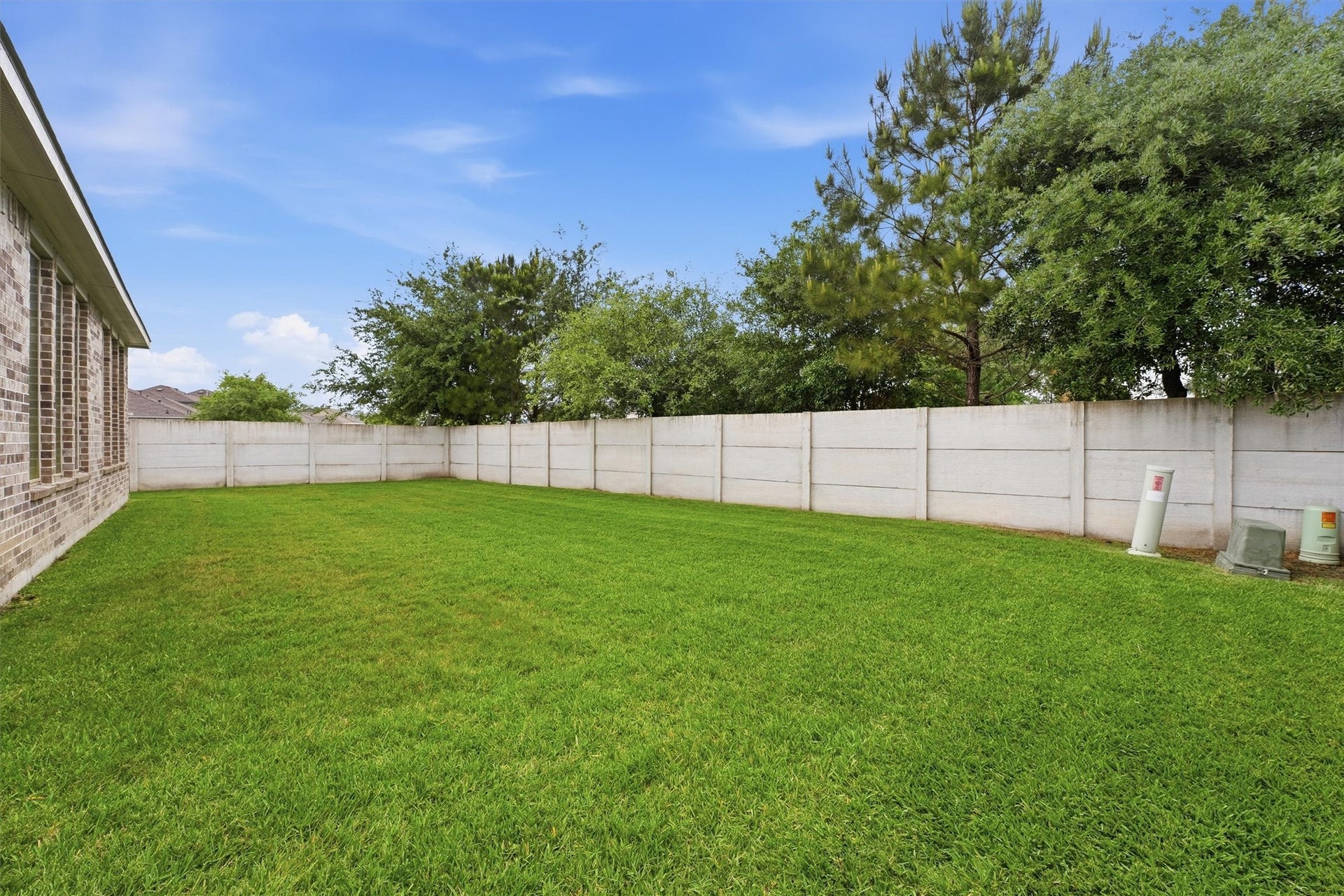 Spacious backyard with lush green grass, bordered by a privacy fence and mature trees, perfect for outdoor activities and relaxation.