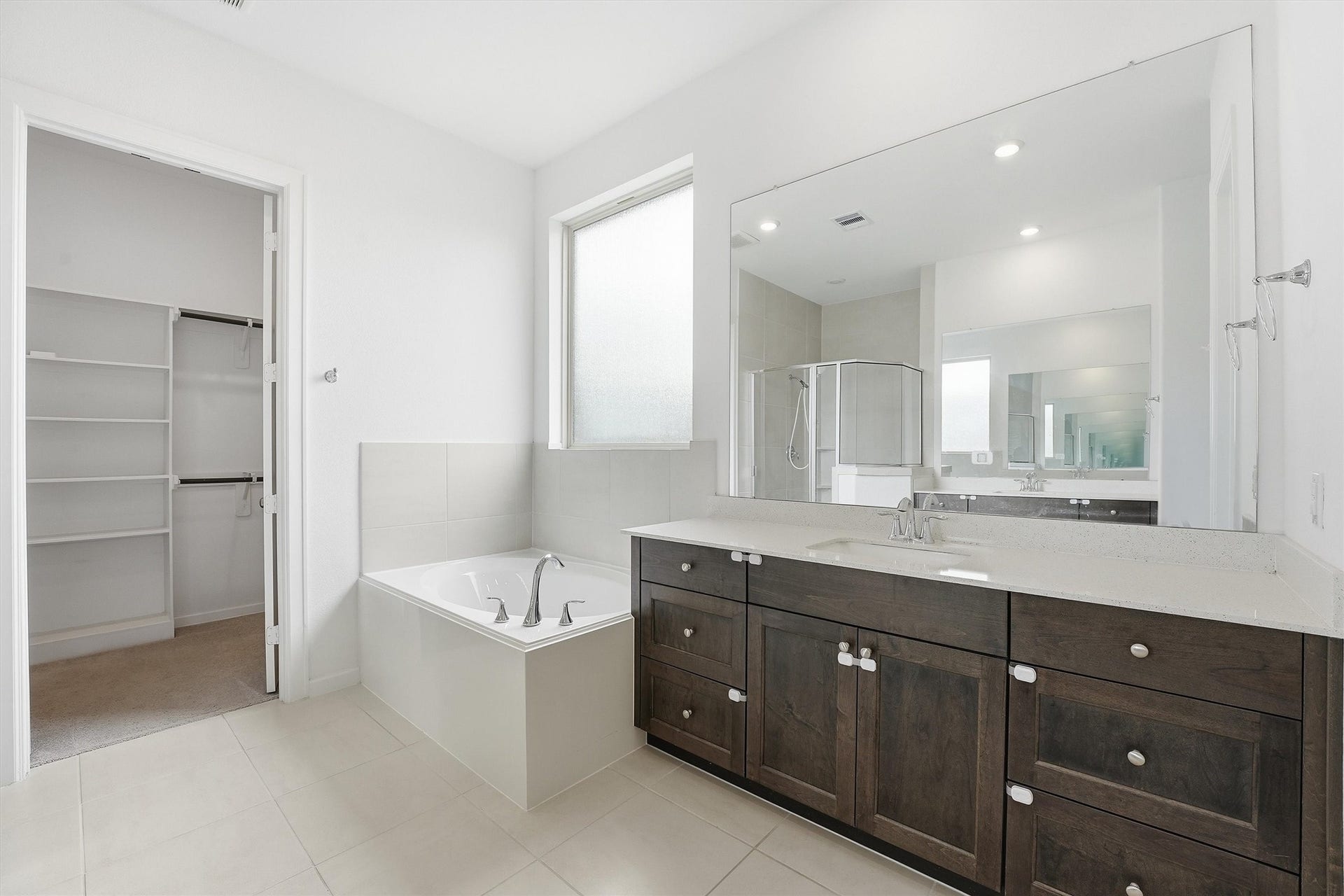 Spacious bathroom featuring a luxurious soaking tub, dual-sink vanity with ample storage, and a glass-enclosed shower, all complemented by modern fixtures and a walk-in closet.
