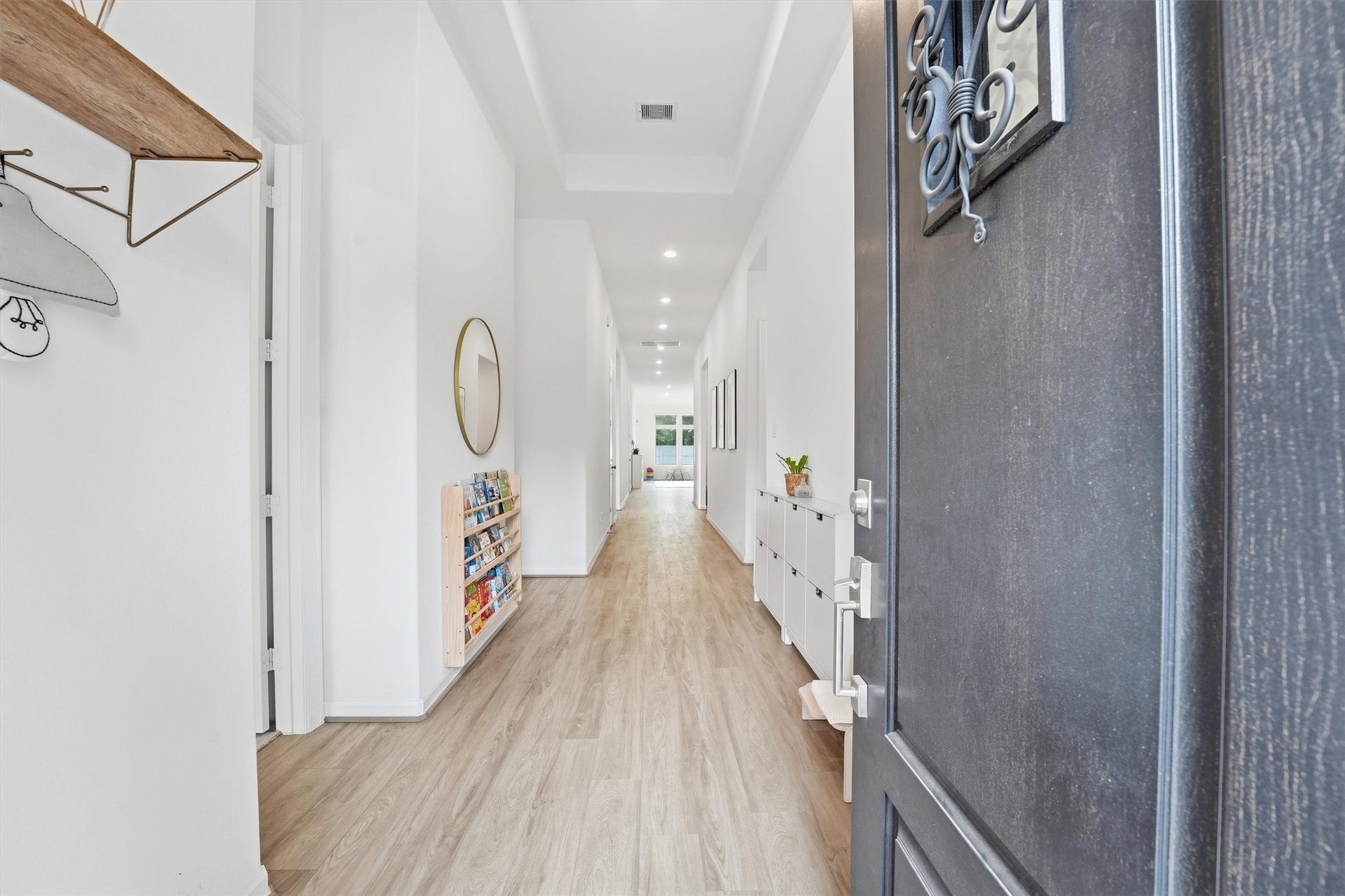 Step into a spacious, light-filled entryway featuring elegant wood-look flooring, sleek white walls, and modern decor, leading to the heart of the home.