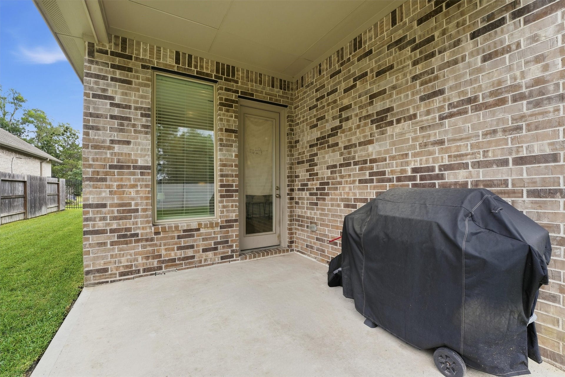 Charming covered patio with brick walls, perfect for outdoor grilling and relaxation with a lush green yard.